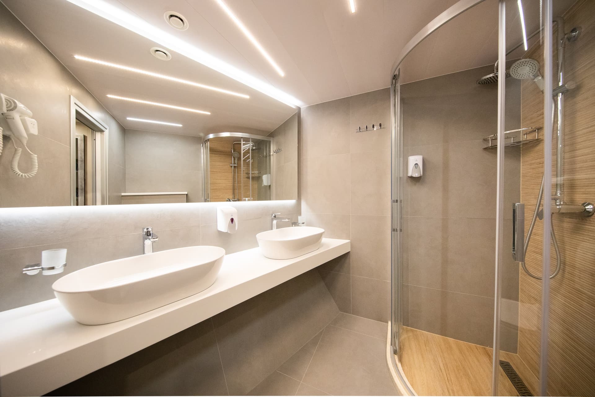 Modern hotel bathroom with double vessel sinks, large illuminated mirror, and glass shower enclosure
