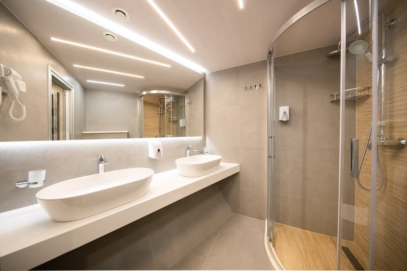 Modern hotel bathroom with double vessel sinks, large illuminated mirror, and glass shower enclosure