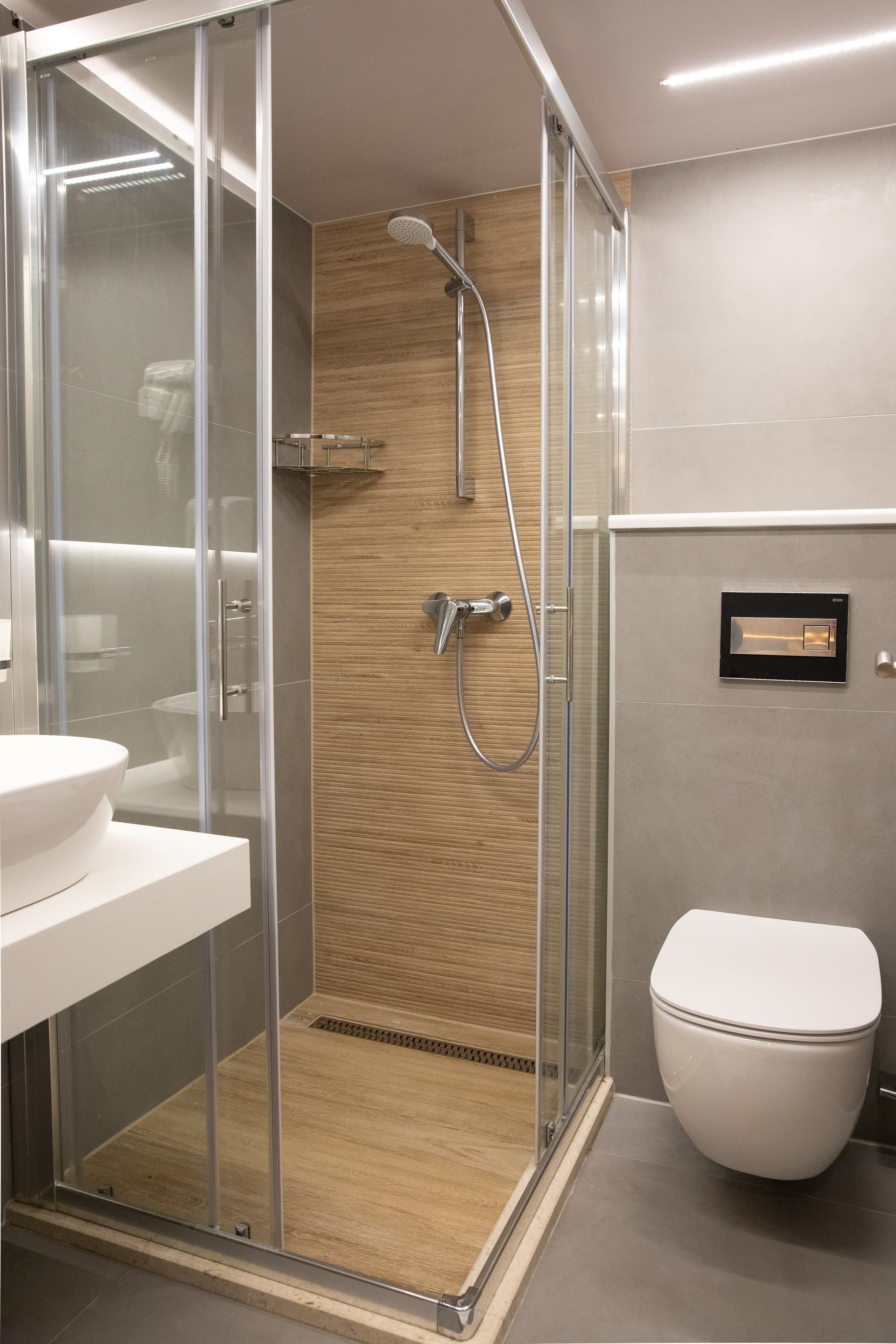 Modern bathroom with glass shower enclosure, wood-look paneling, and wall-hung toilet