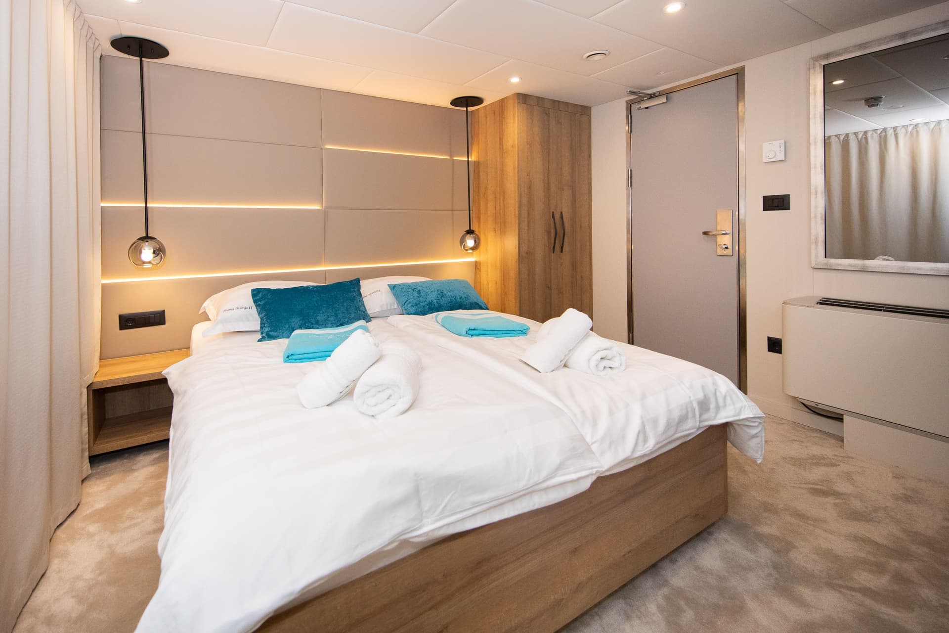 Modern cabin bedroom with double bed, white linens, blue pillows, and pendant lights