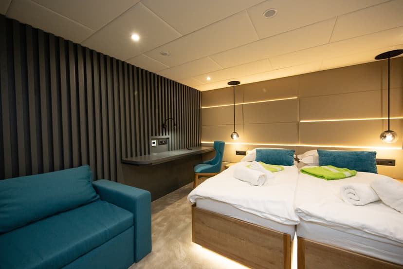 Modern hotel cabin interior with twin beds, blue sofa, and desk area
