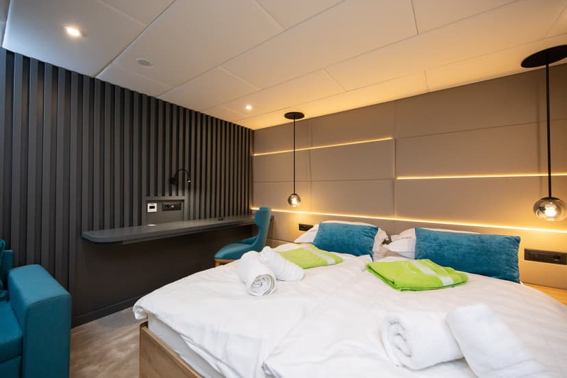 Modern hotel room interior with twin beds, blue pillows, rolled white towels, and ambient lighting.