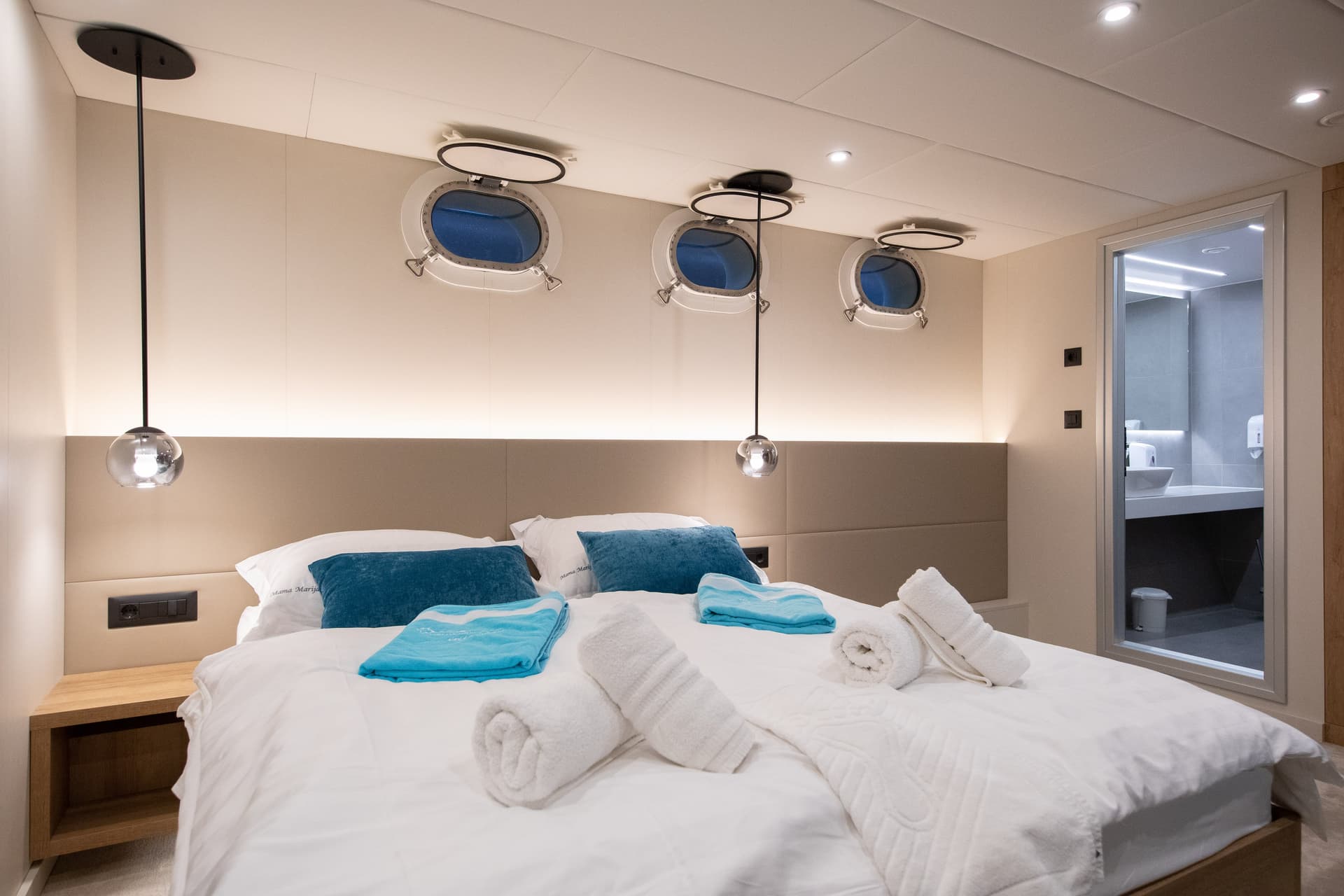 Modern cabin bedroom with white linens, blue pillows, and portholes on the wall