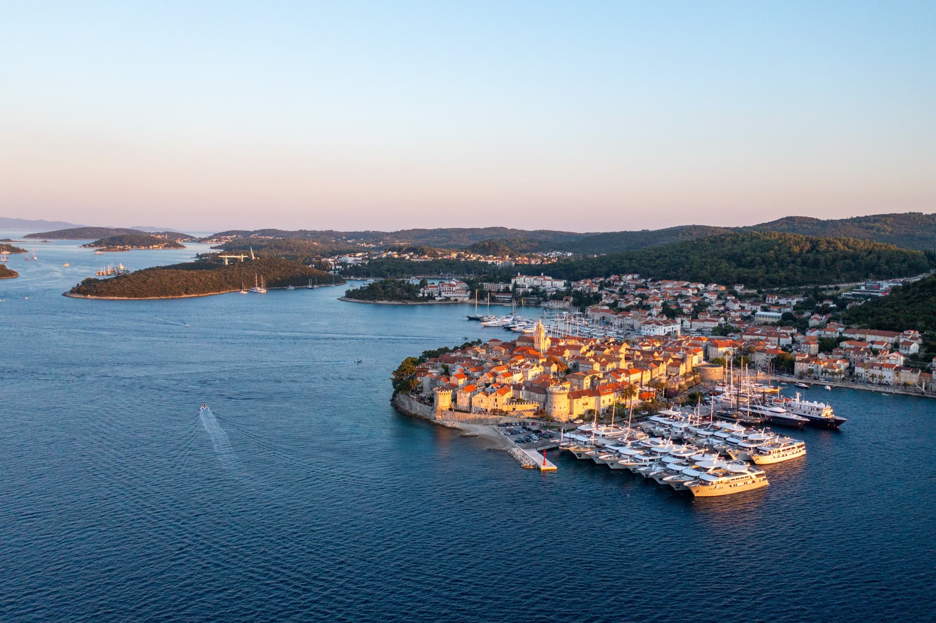 Coastal town with marina and docked yachts along blue sea at sunset