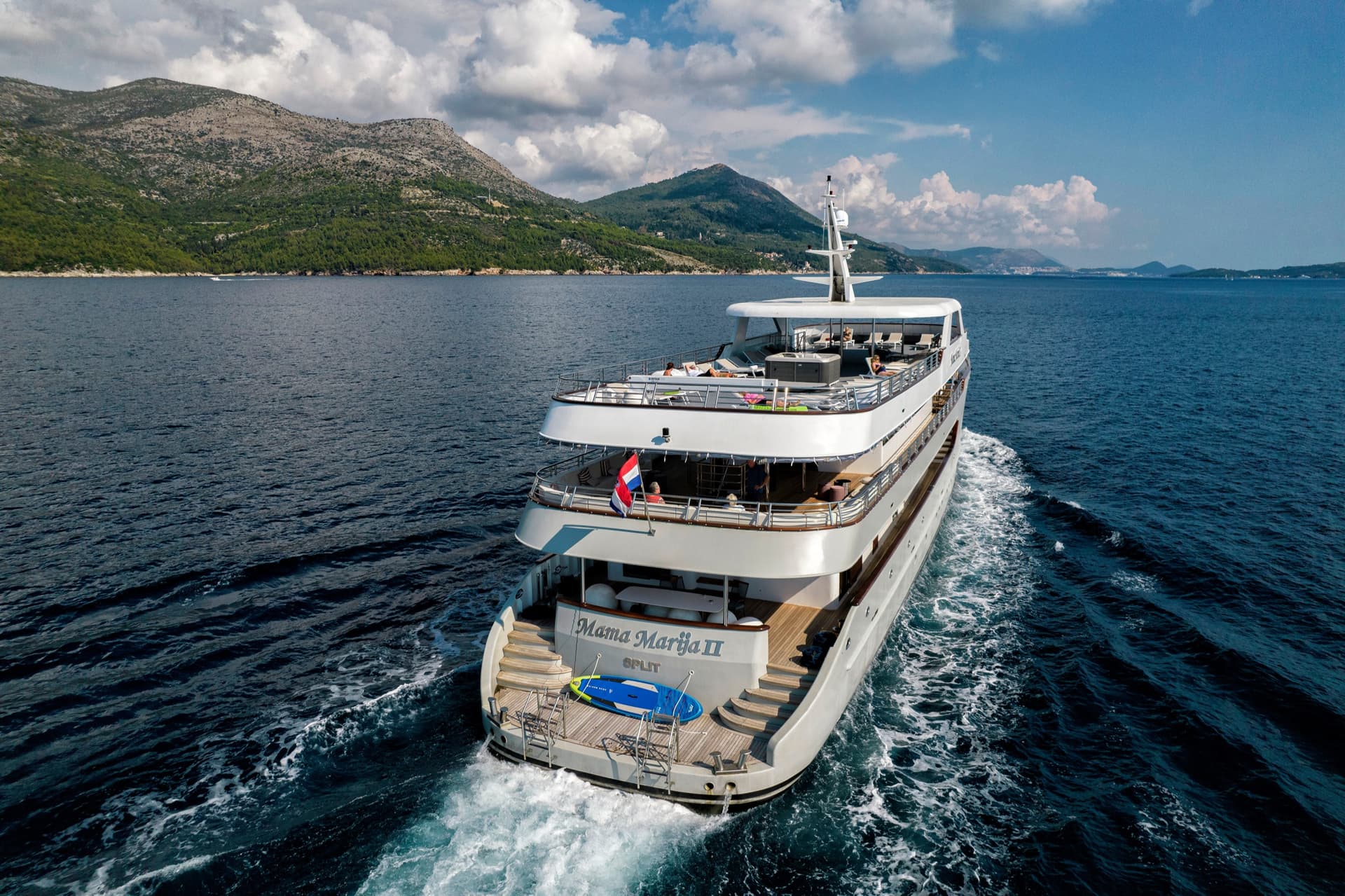 Yacht cruising on calm blue sea with mountainous coastline in background