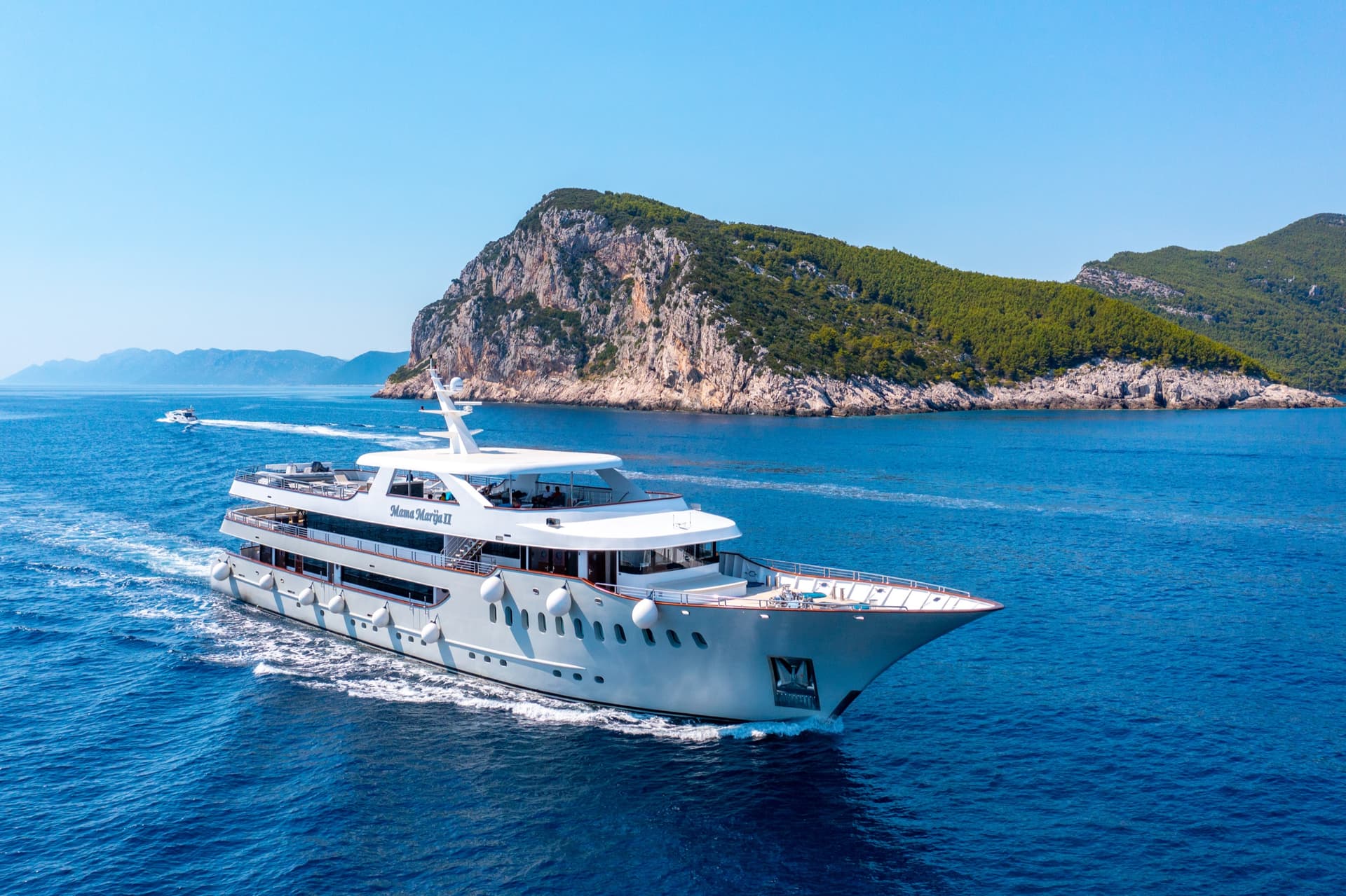 Luxury yacht cruising on blue coastal waters past rocky island
