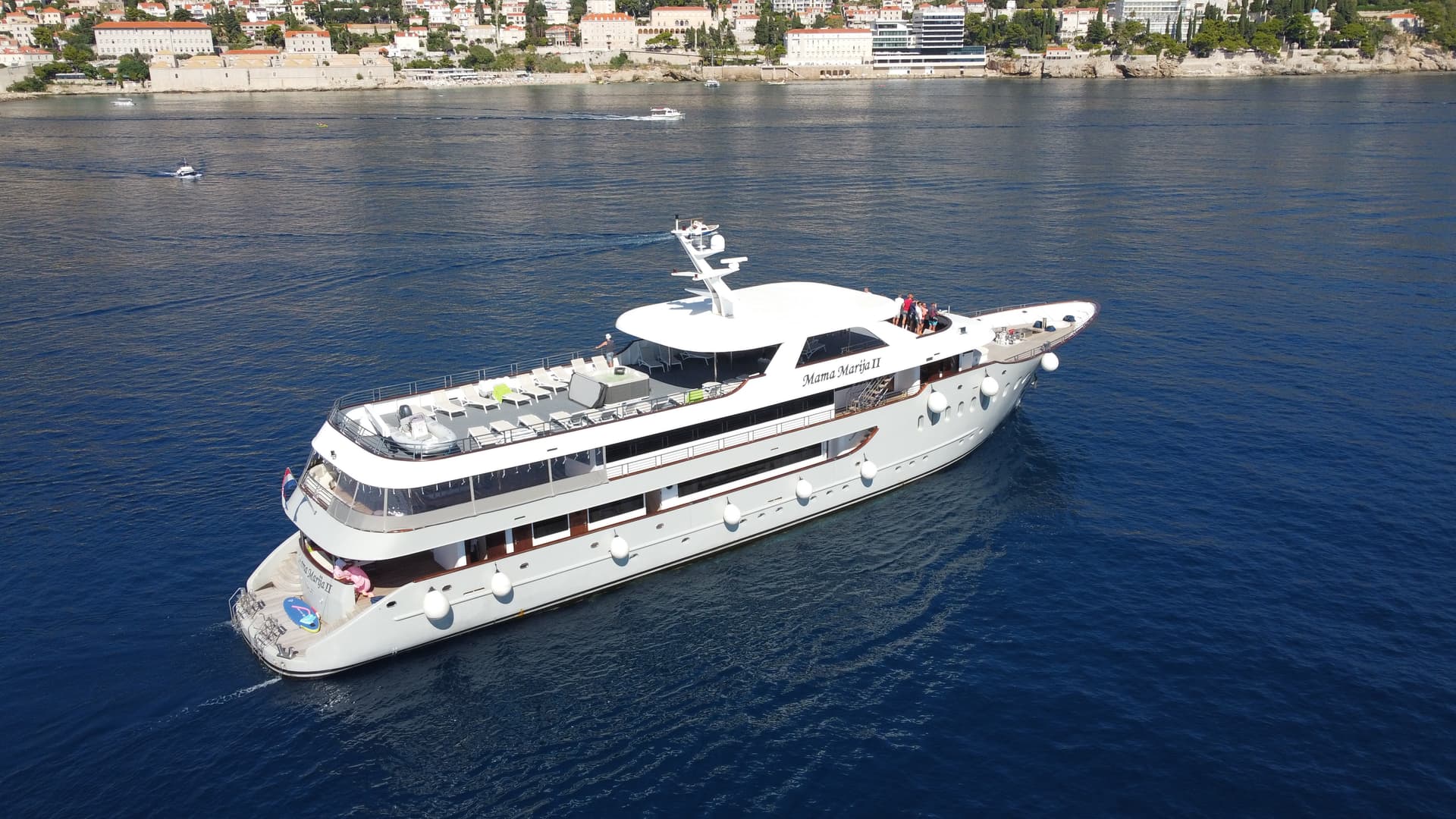 Large white yacht cruising on blue coastal waters with buildings in background