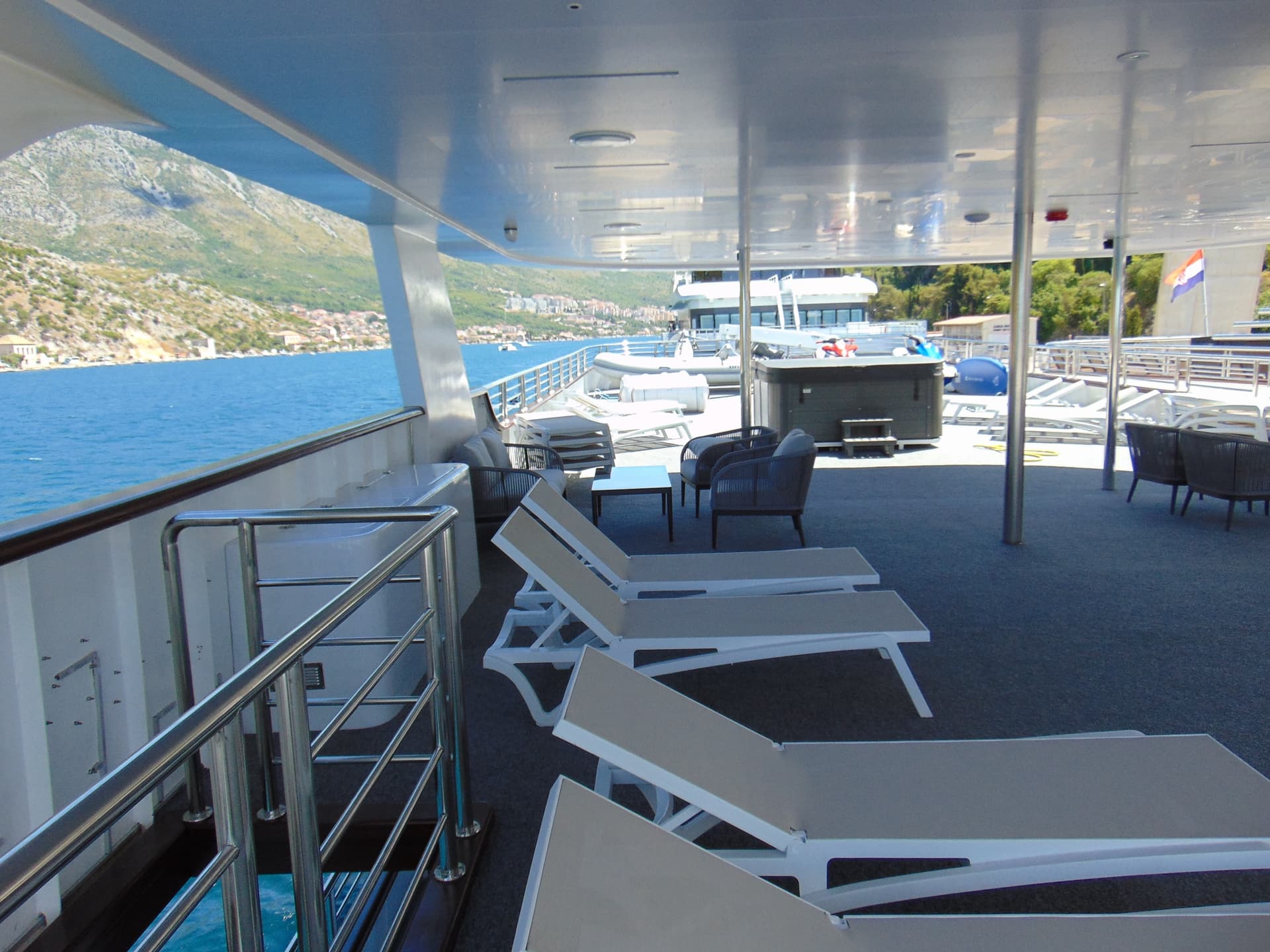 Yacht deck with lounge chairs and hot tub overlooking coastal mountains