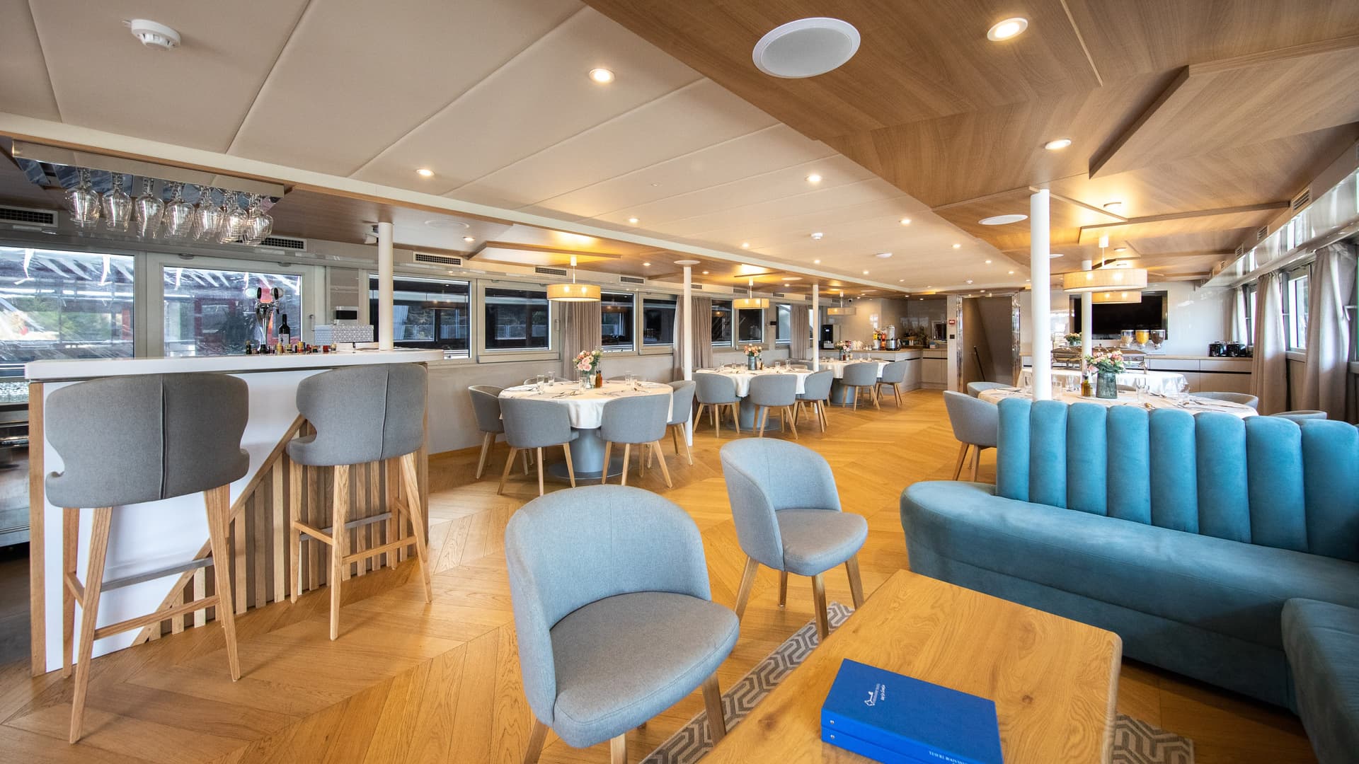 Modern restaurant and lobby interior with wooden flooring, gray armchairs, and dining tables