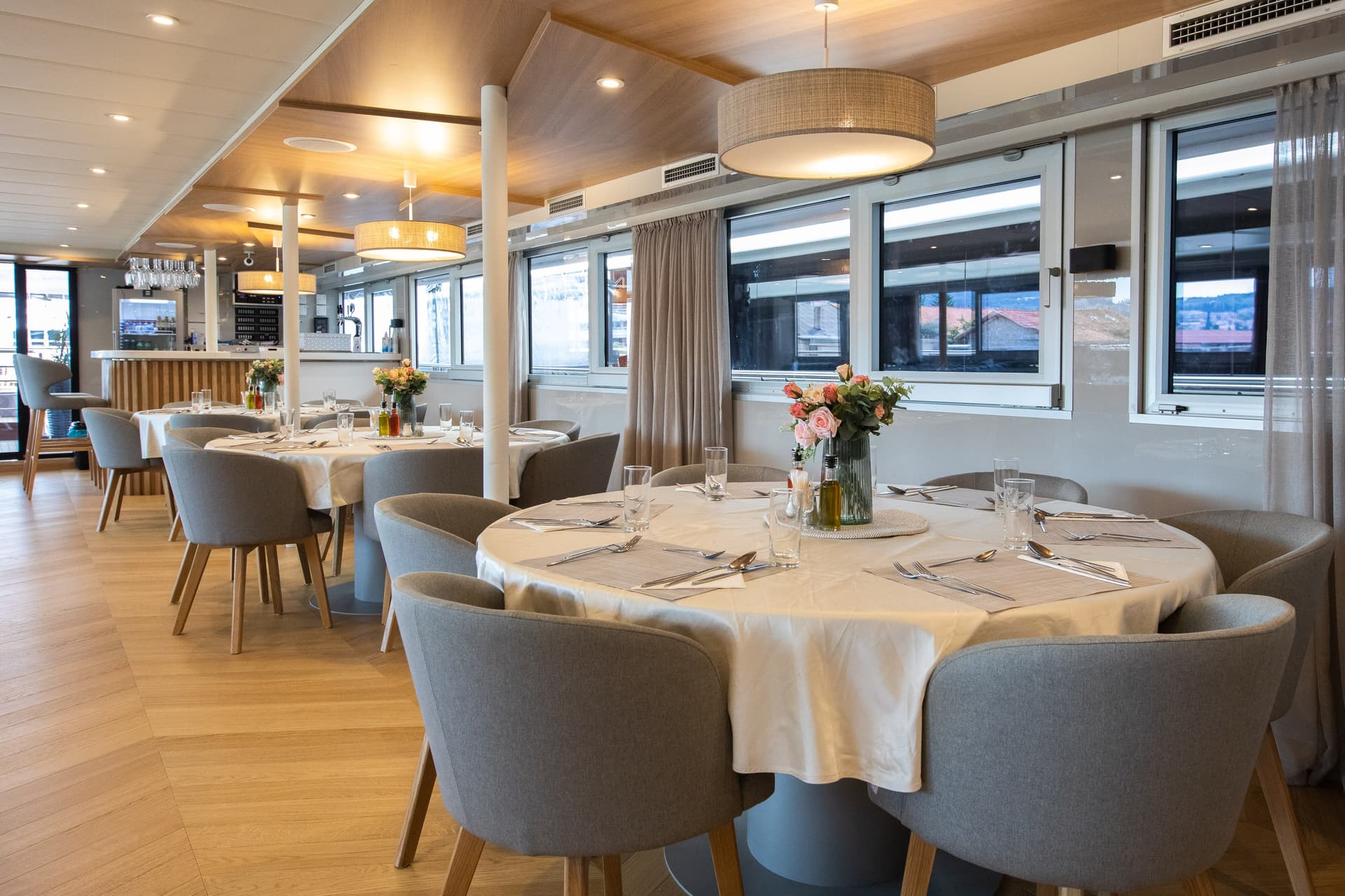 Restaurant dining area with round tables, place settings, and gray armchairs inside a modern interior space