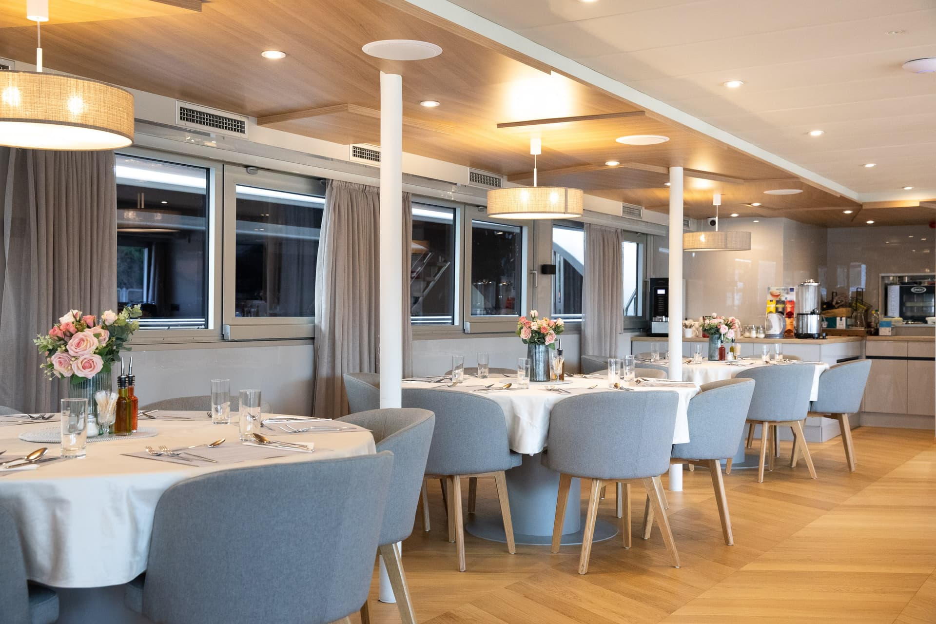 Restaurant interior with set dining tables, grey armchairs, and wood-paneled ceiling