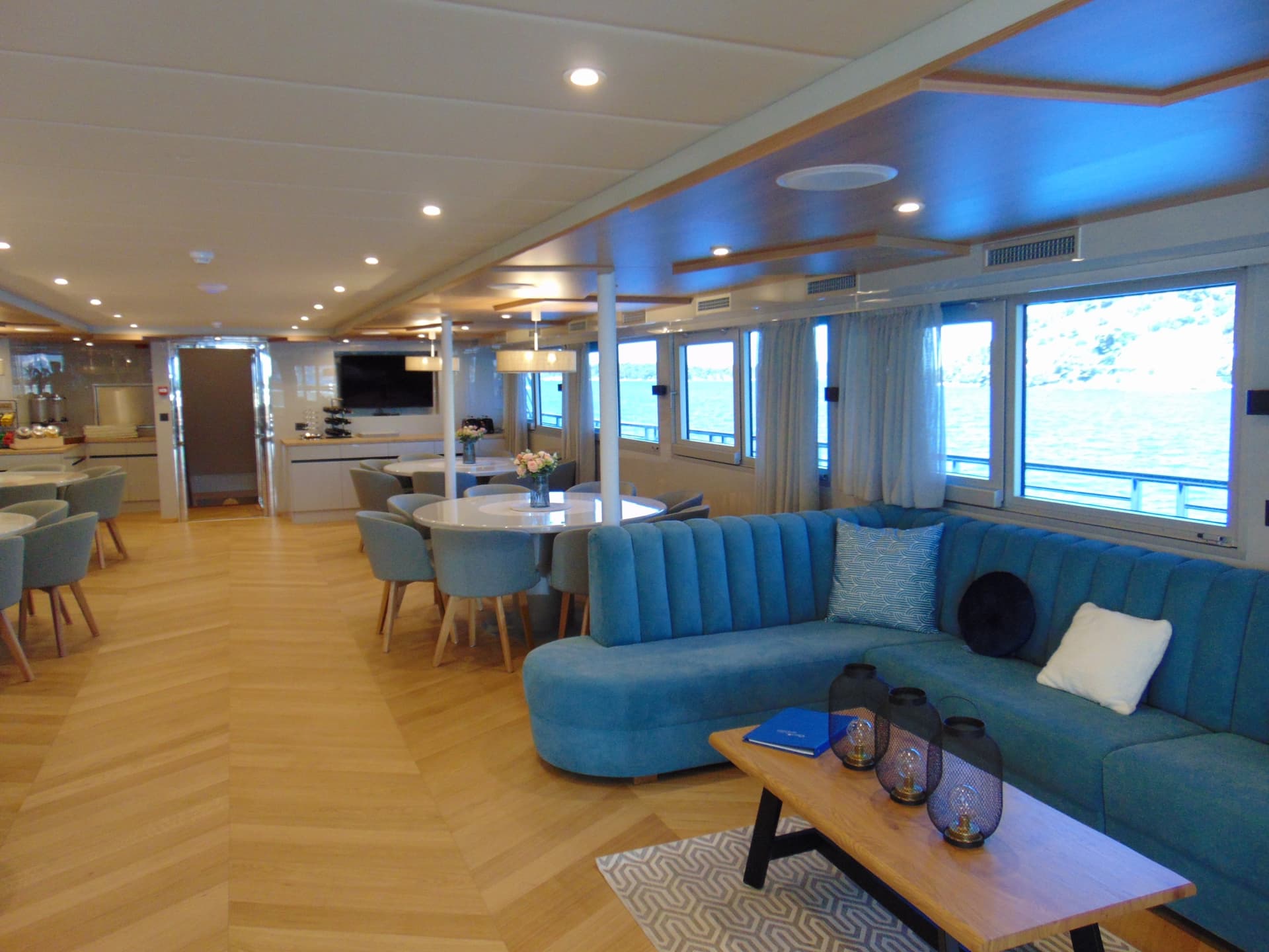 Modern yacht lounge and dining area with blue sectional sofa and large windows overlooking water