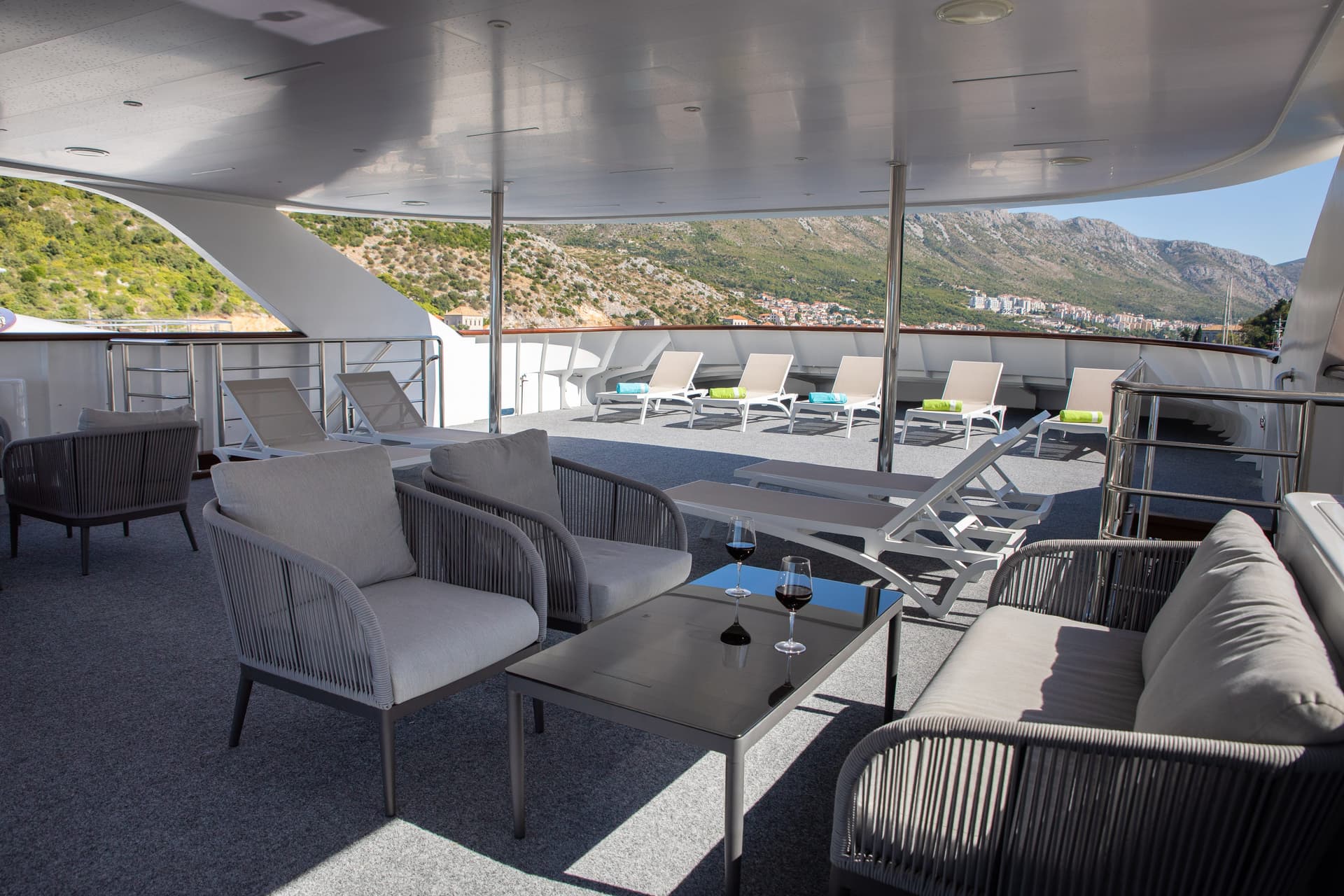 Yacht sun deck with lounge seating and armchairs overlooking coastal mountains
