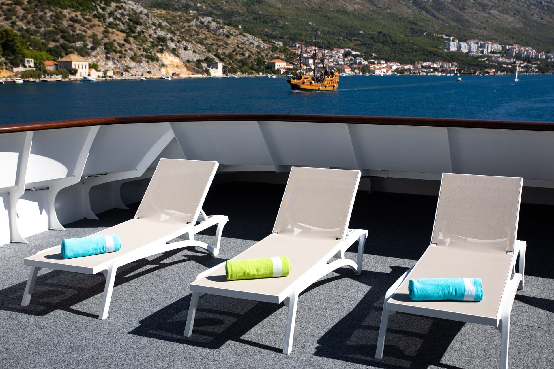 Sun loungers with rolled towels on a sunny ship deck overlooking coastal waters and mountains