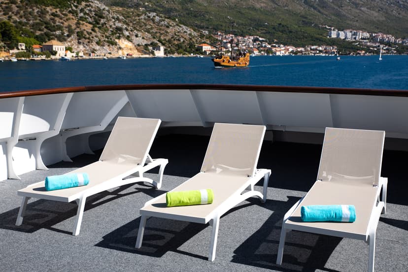 Sun loungers with rolled towels on a sunny ship deck overlooking coastal waters and mountains