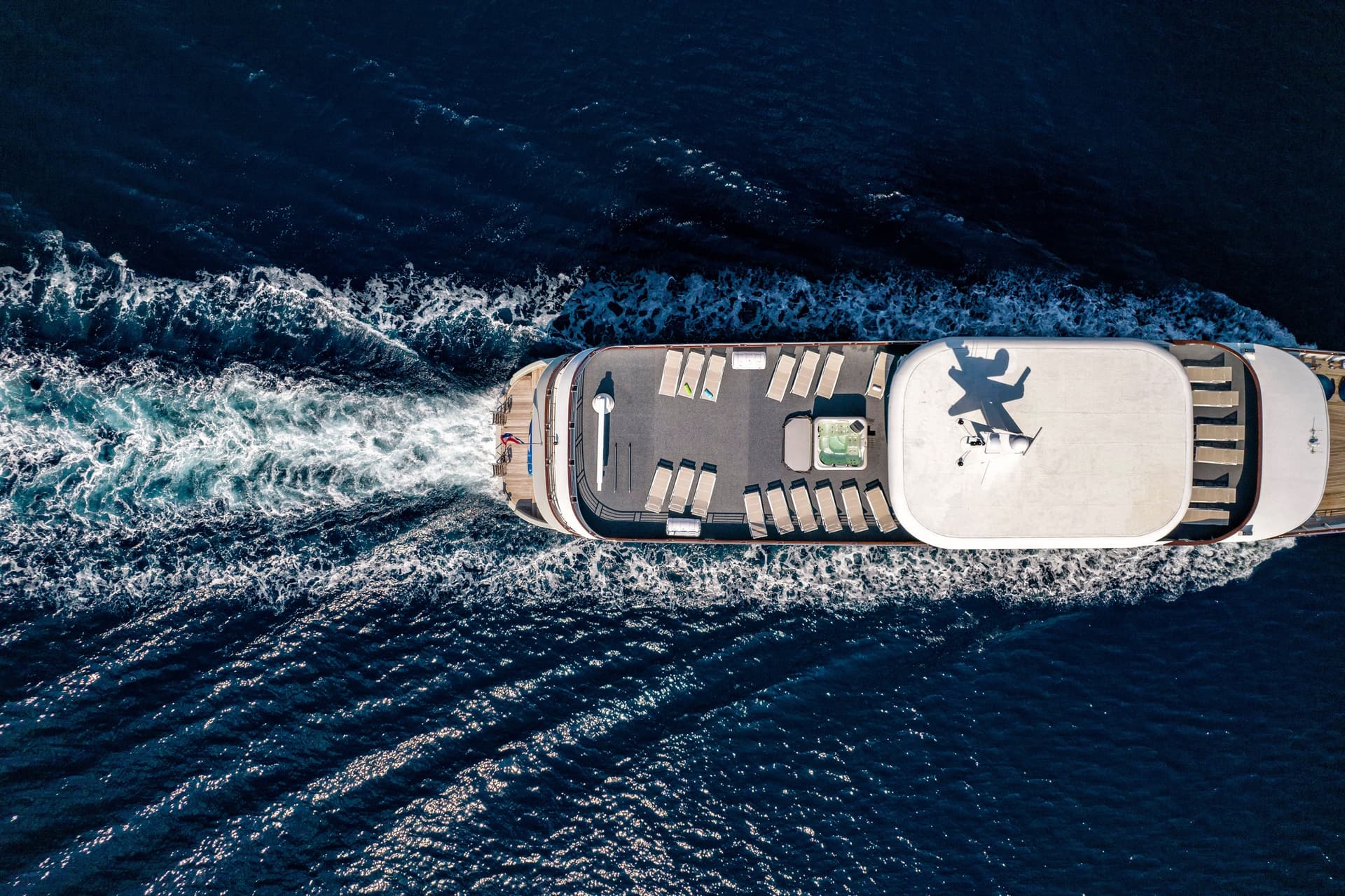 Aerial view of a yacht cruising on deep blue sea water with sun loungers on deck