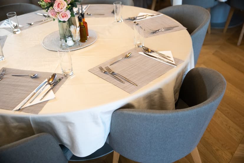 Round dining table set with place settings, cutlery, glasses, and floral centerpiece in restaurant