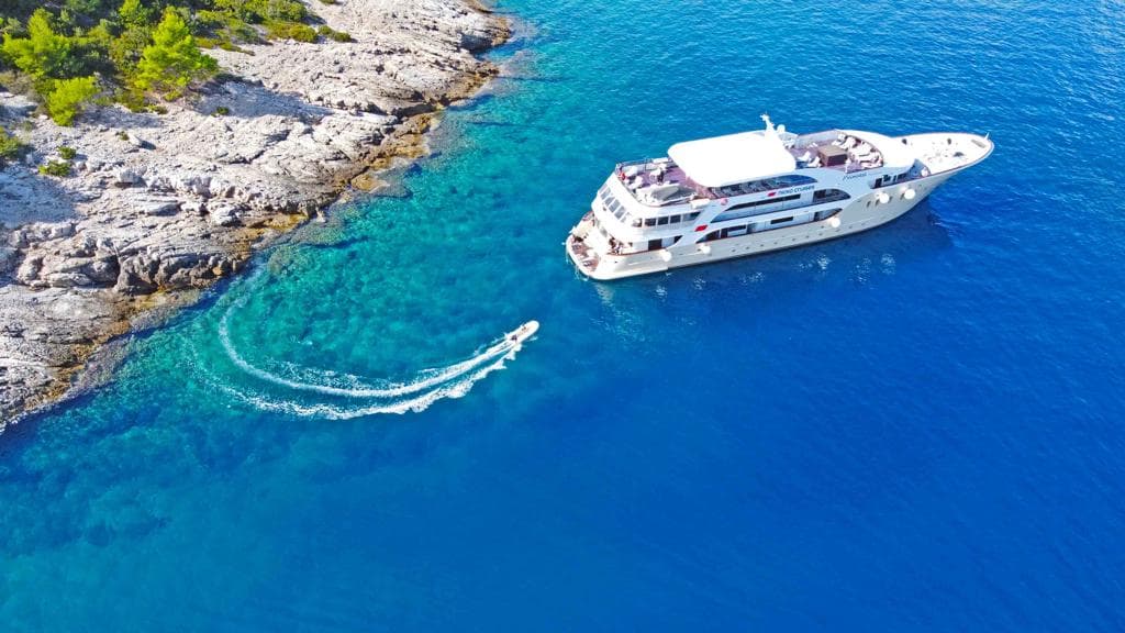 Yacht and small tender boat on blue coastal waters near rocky shoreline