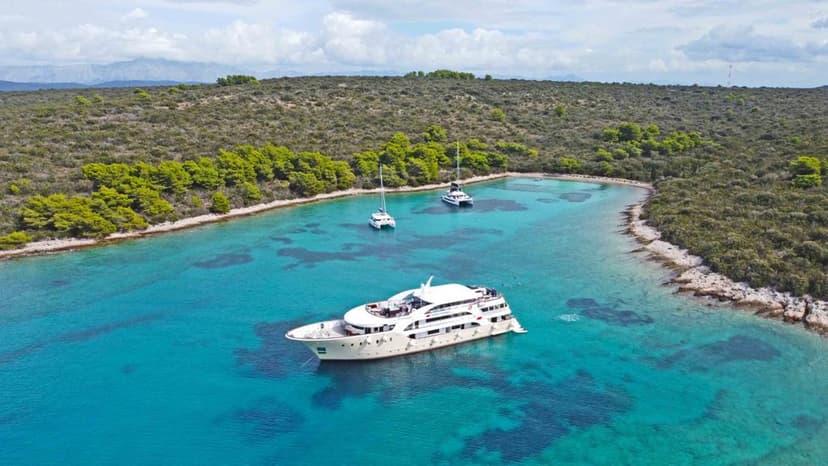 Yacht anchored in turquoise coastal bay with green forested hills