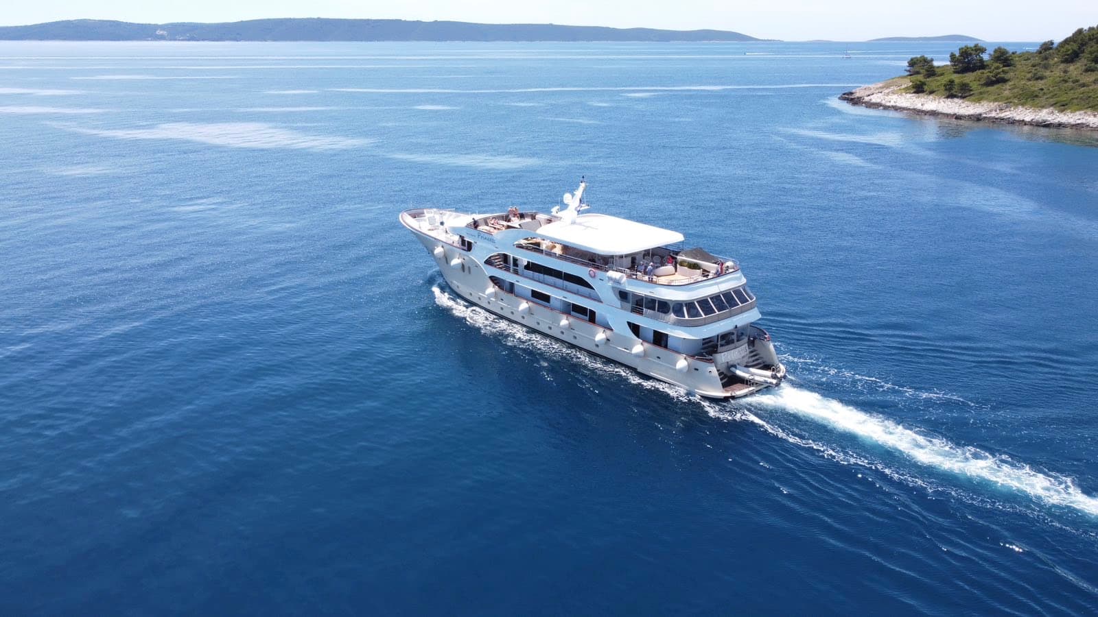 Large yacht cruising on blue coastal waters near an island