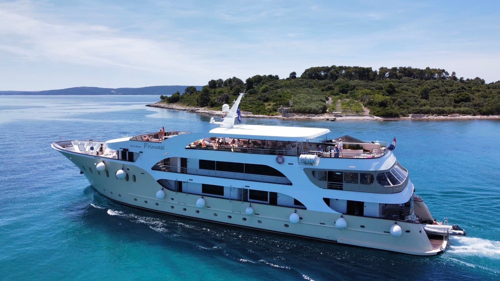 Large cruise yacht sailing on blue coastal waters near a forested island