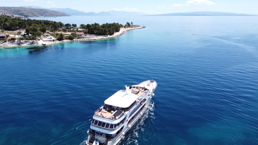 Yacht sailing on blue coastal waters near a forested coastline
