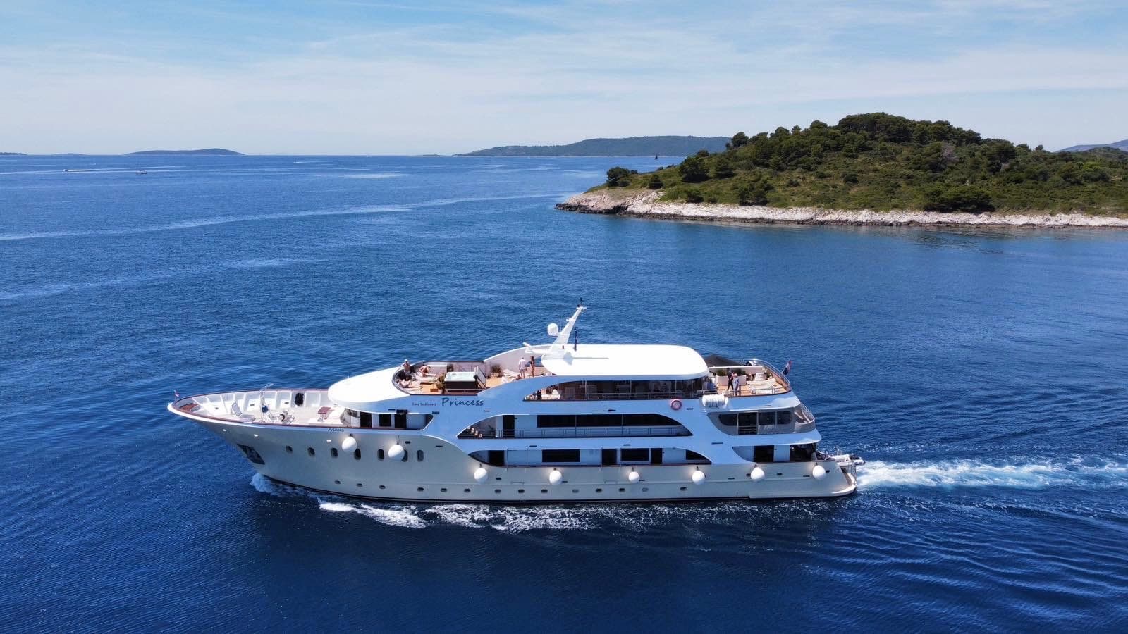 Large white yacht cruising on blue coastal waters past green islands