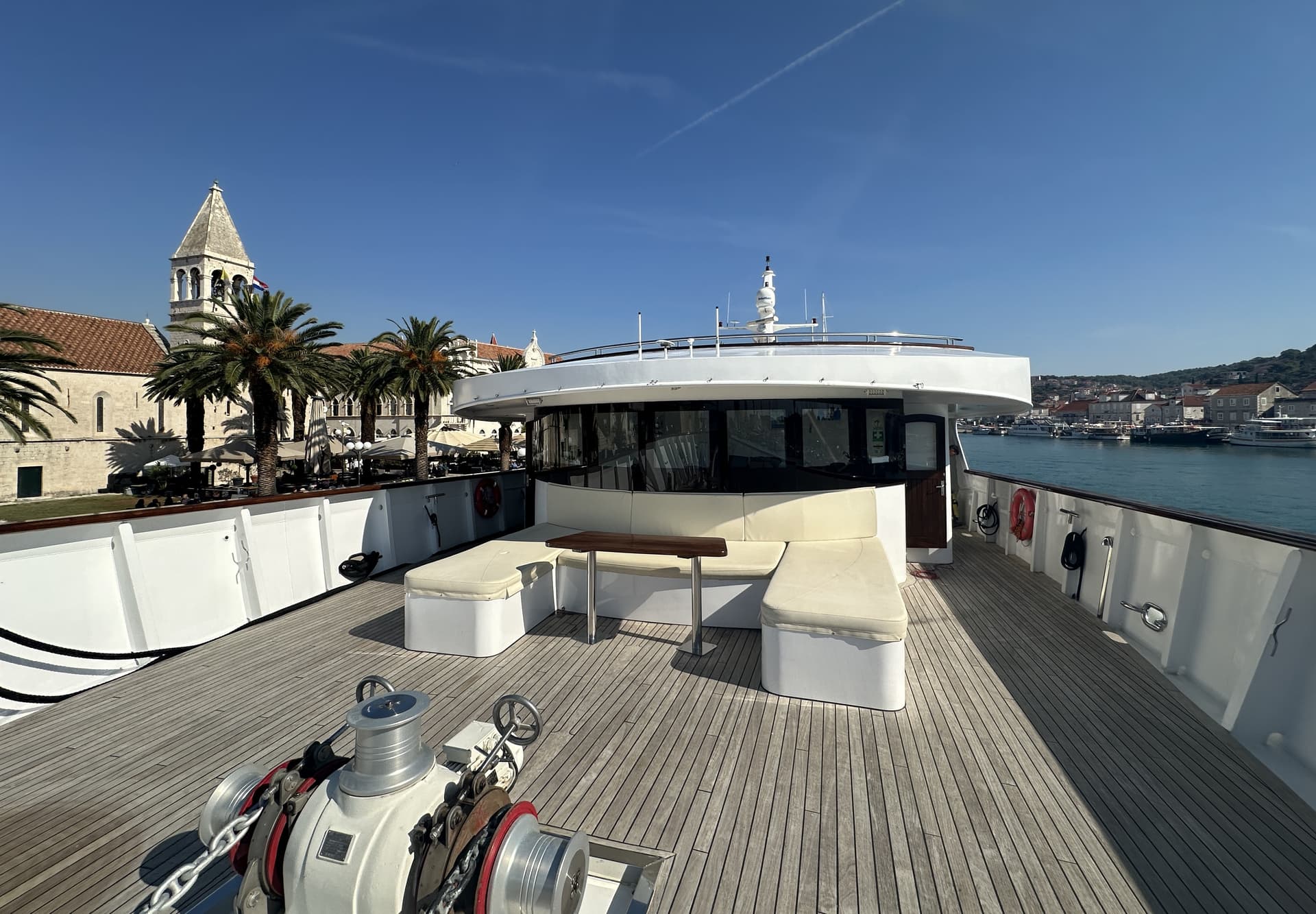 Yacht deck with seating area and wooden flooring docked in harbor with historic buildings