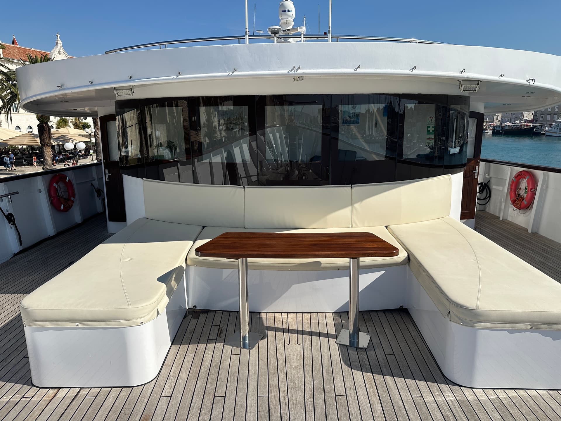Yacht deck with curved white seating and wooden table in harbor
