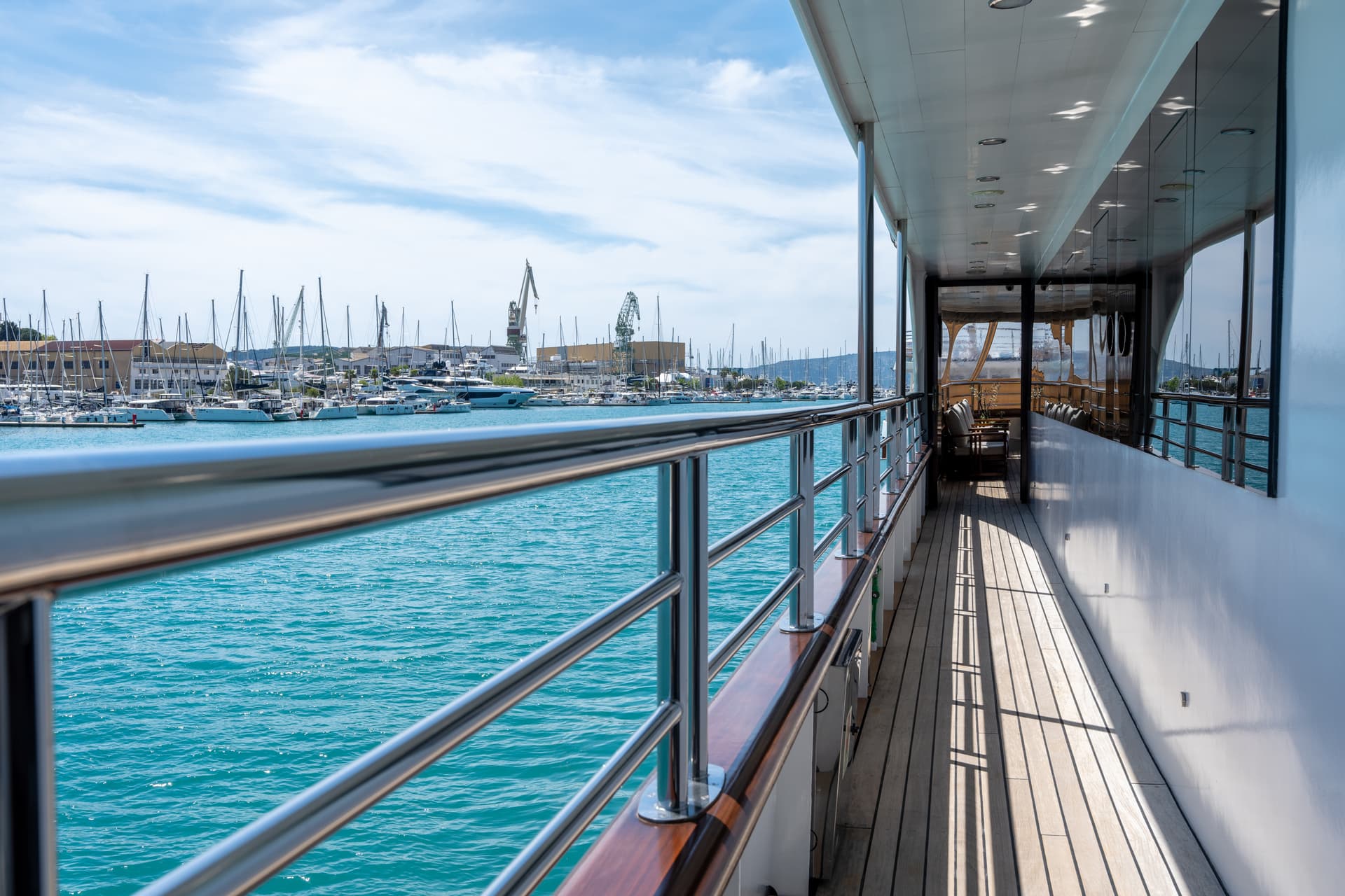 Yacht deck with wooden flooring and metal railing overlooking a marina with boats