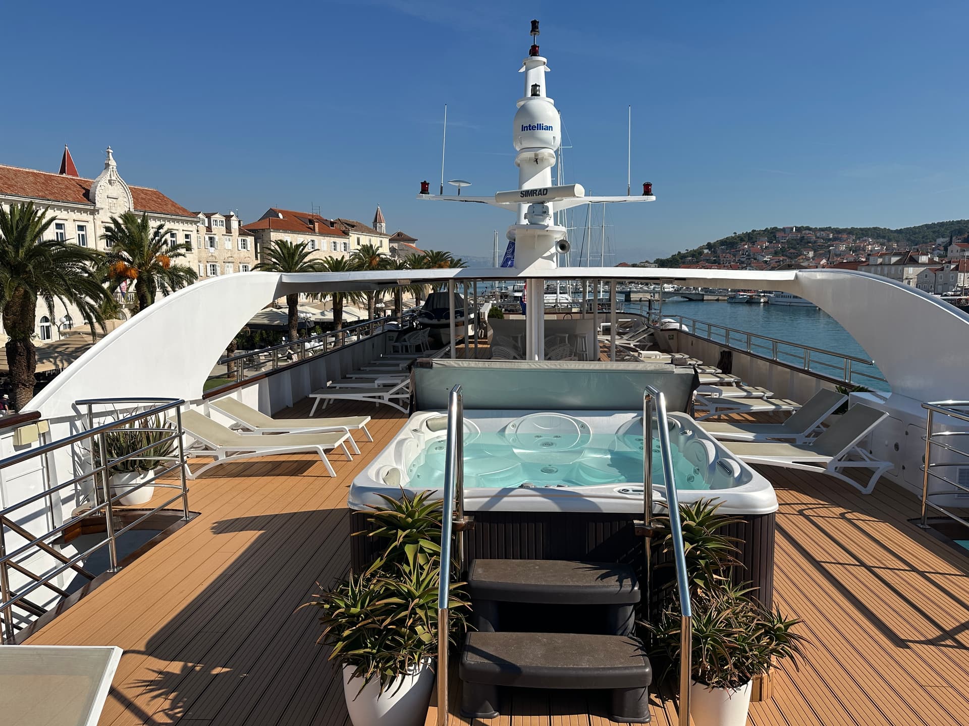 Yacht sun deck with hot tub, lounge chairs, and coastal town backdrop