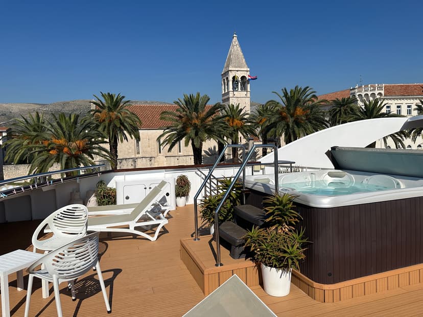 Sun deck with hot tub, loungers, and chairs overlooking a town with palm trees and a bell tower