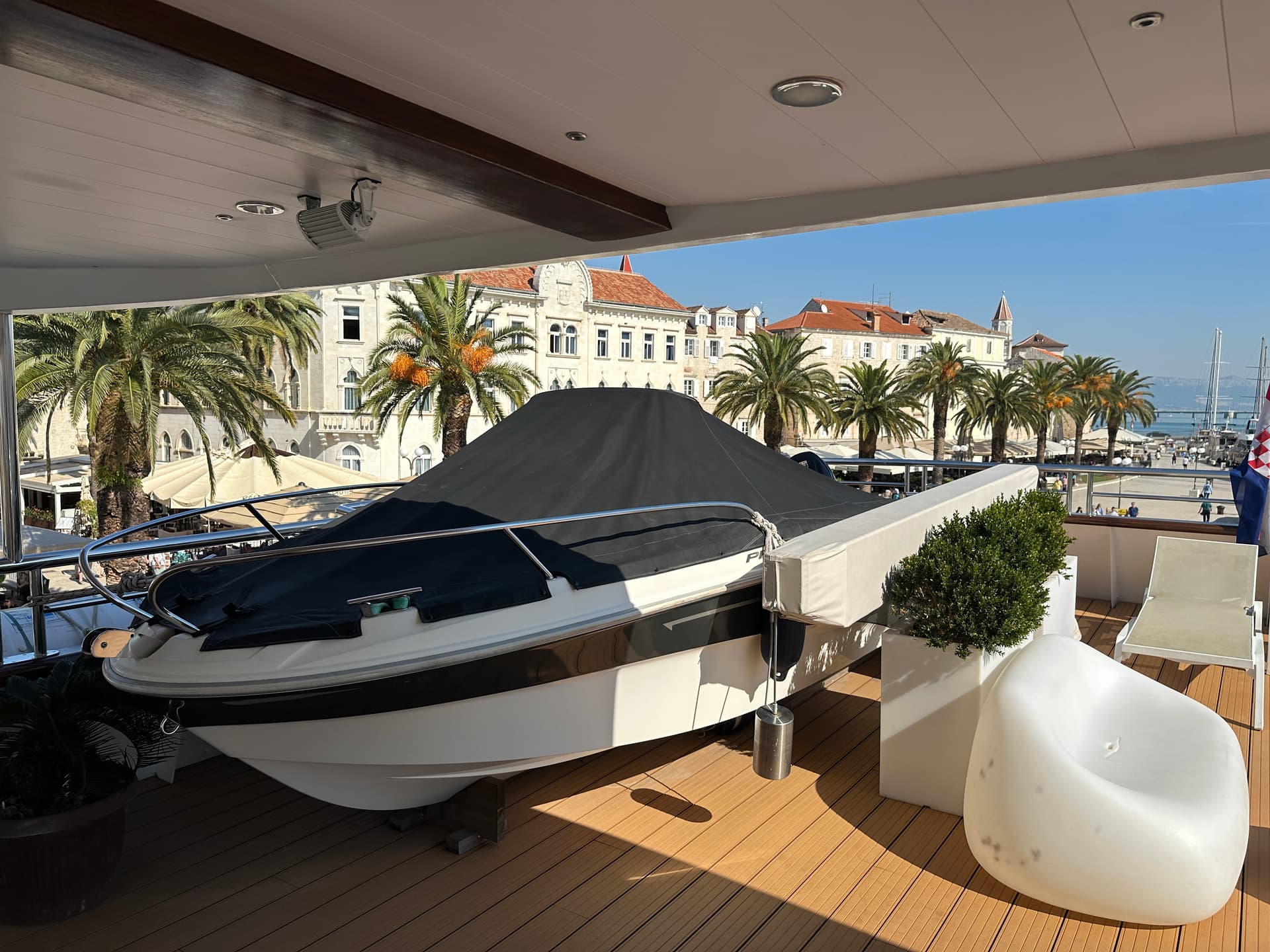 Covered motorboat on sunny deck with palm trees and waterfront buildings in background