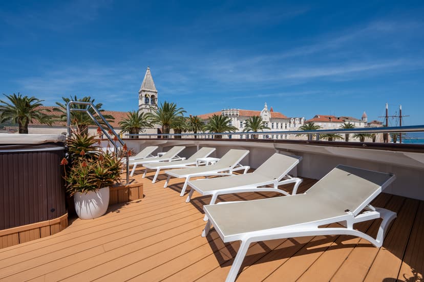 Sun deck with lounge chairs and potted plants on a yacht with coastal town backdrop
