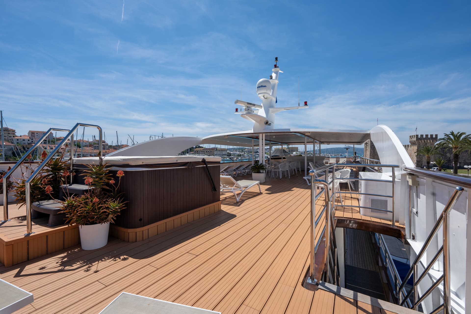 Sunny yacht deck with wooden flooring, hot tub, and lounge chairs under a blue sky