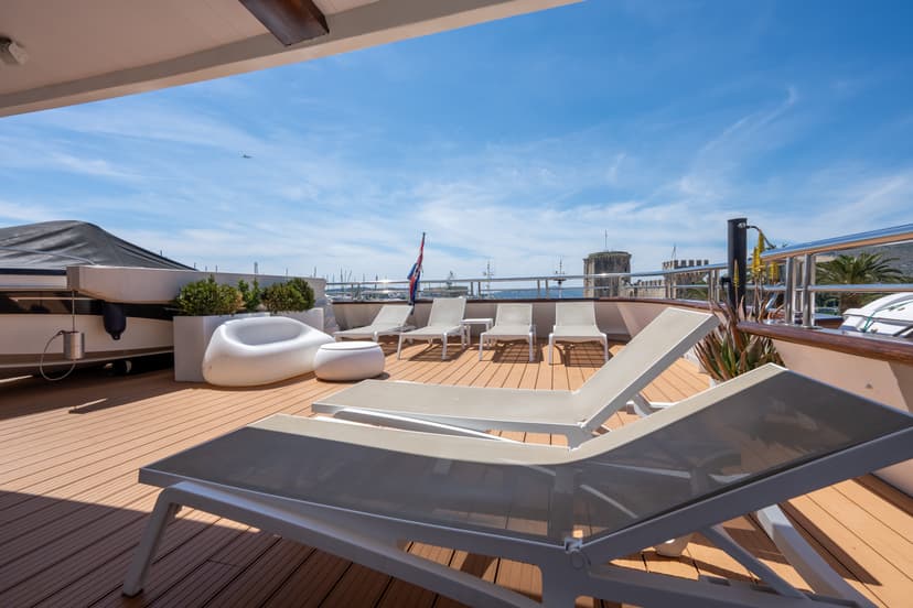 Sunny yacht deck with lounge chairs and seating area overlooking a harbor with stone fortress