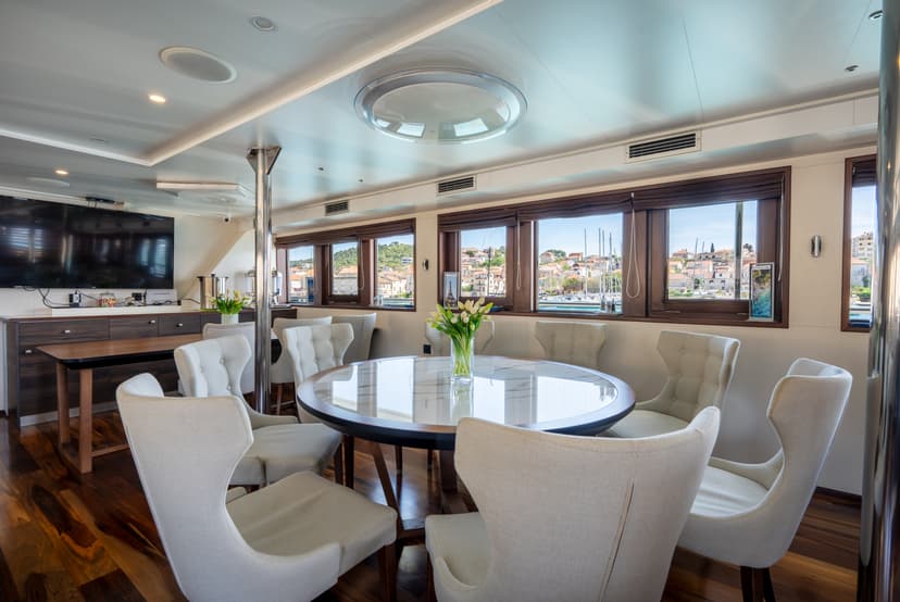 Modern yacht dining area with round table and white chairs overlooking coastal town through windows