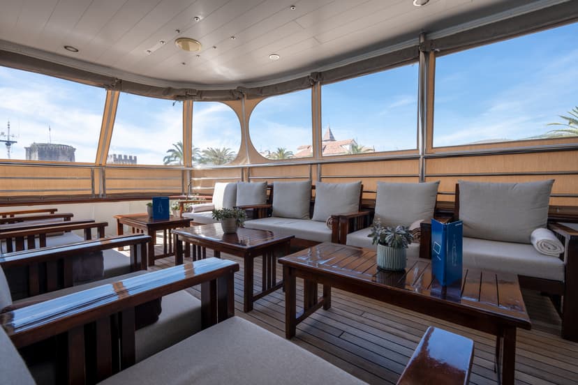 Lobby bar lounge area with wooden furniture and large windows on a boat deck