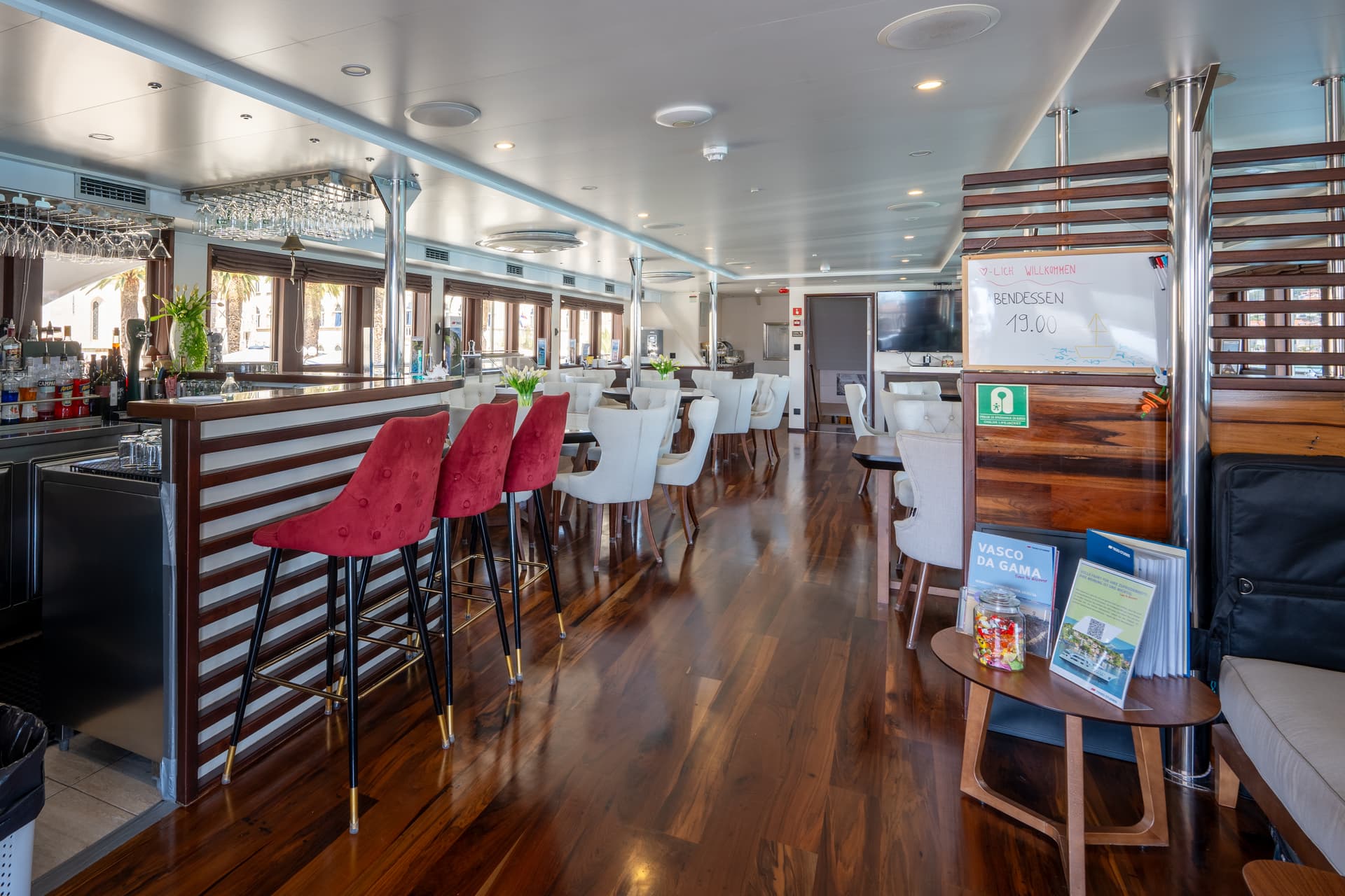 Modern restaurant and lobby bar interior with red and white bar stools on hardwood floors.