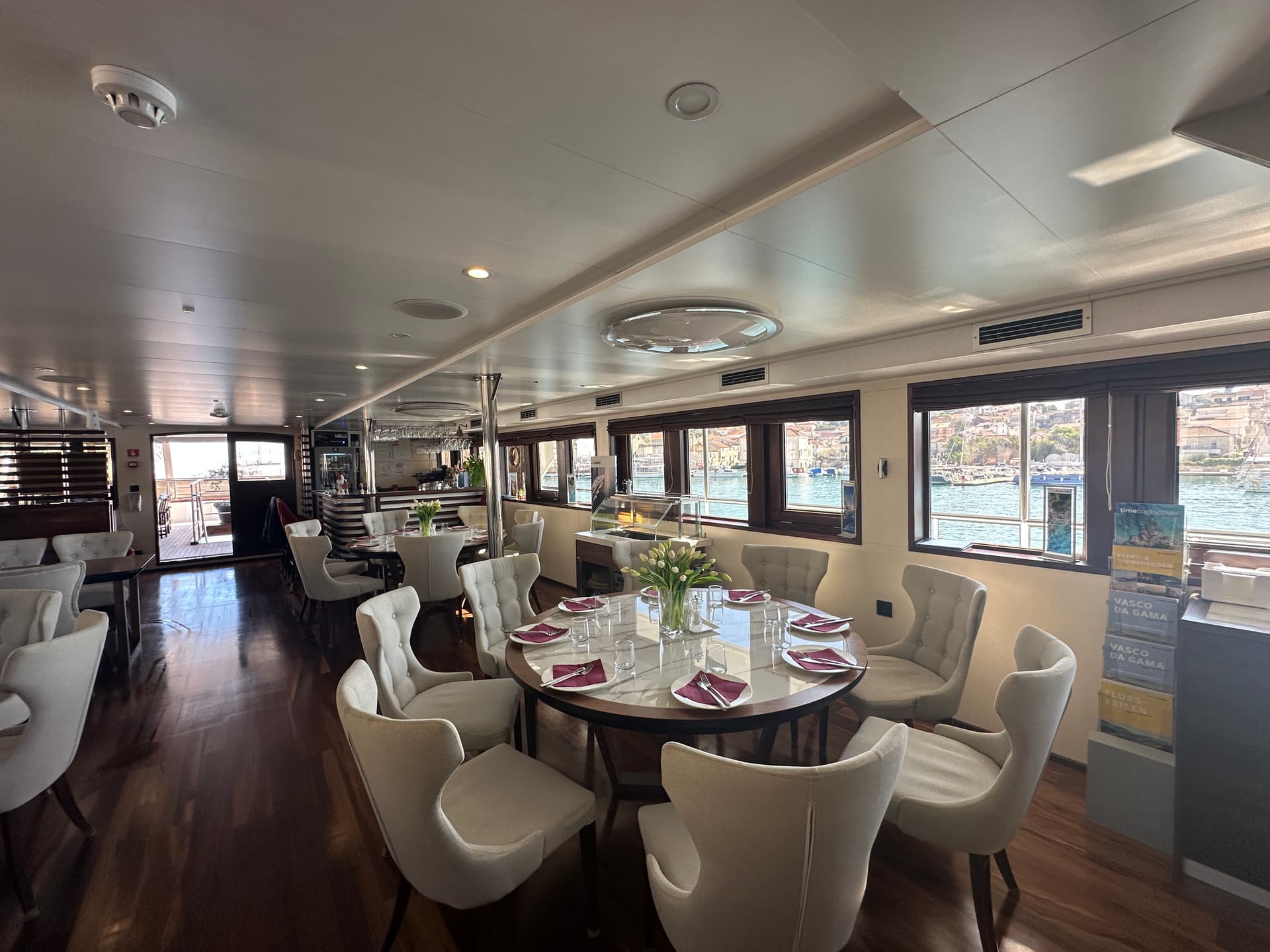 Restaurant interior with set dining tables and large windows overlooking water and coastal town