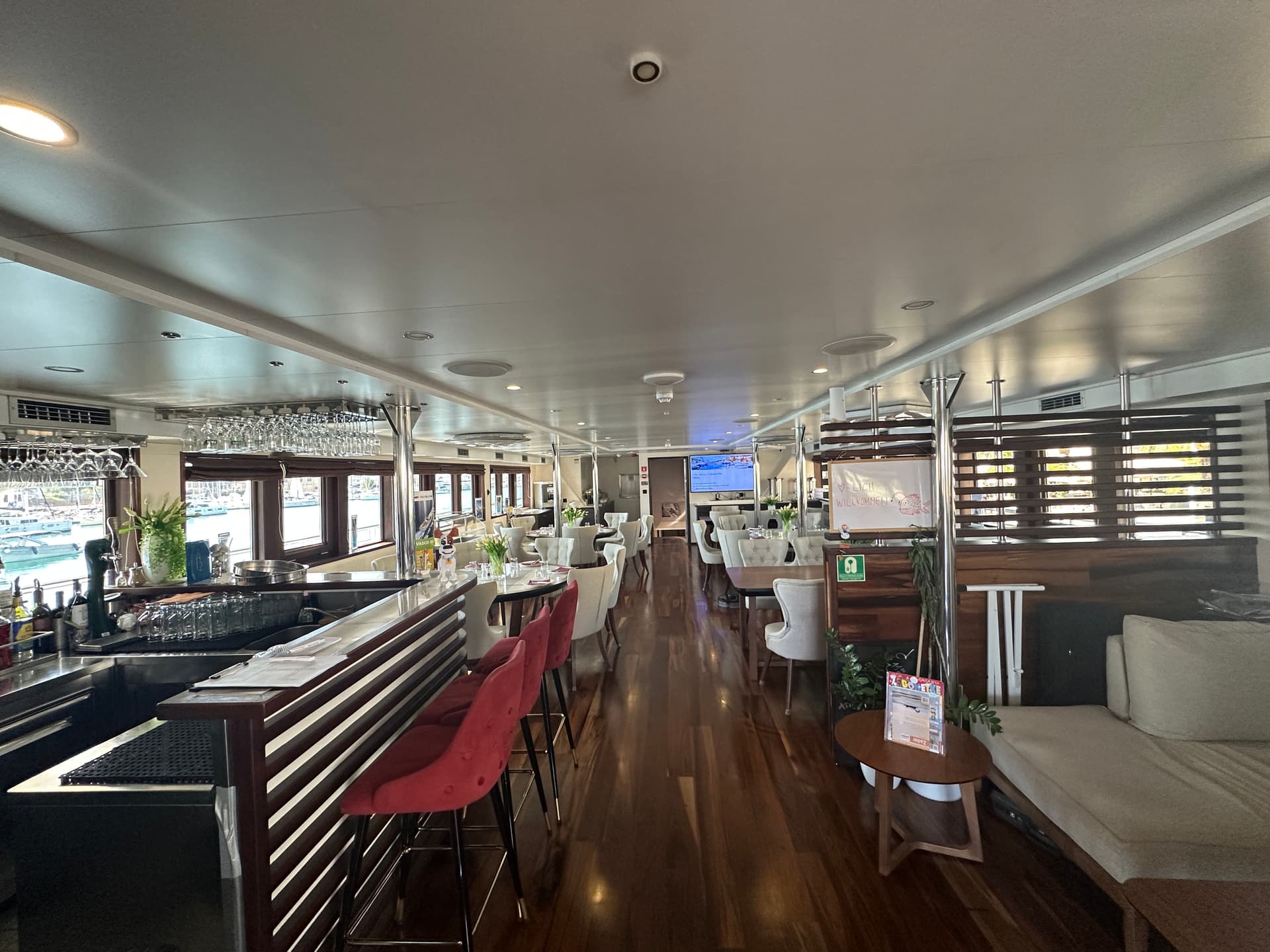 Restaurant and lobby bar interior with a bar counter, red bar stools, wooden flooring, and dining seating area.