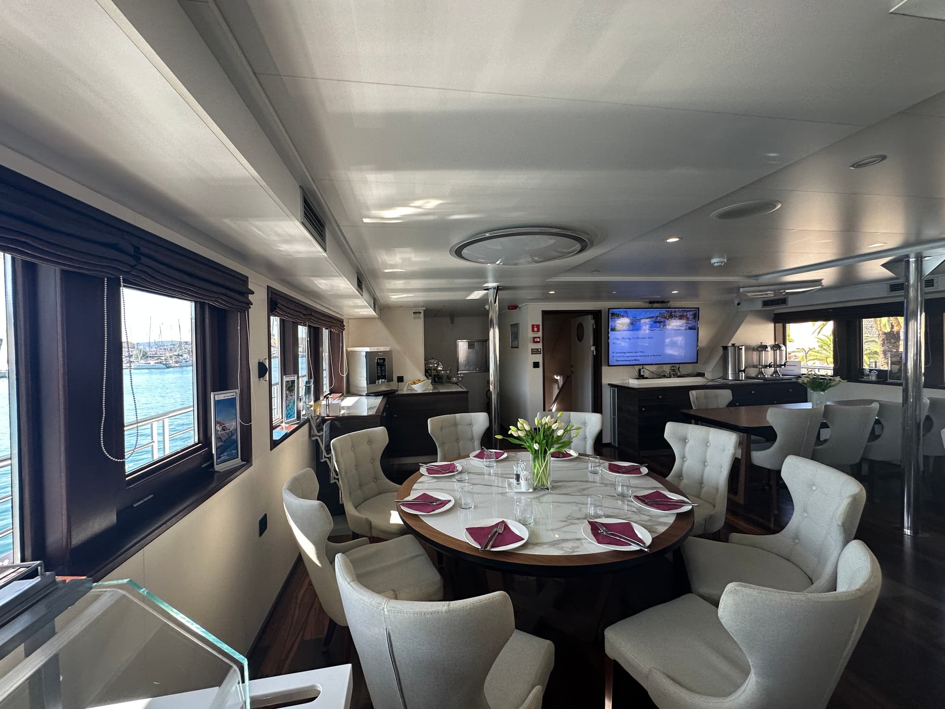 Restaurant and lobby bar interior with round dining table, upholstered chairs, and large windows overlooking the harbor