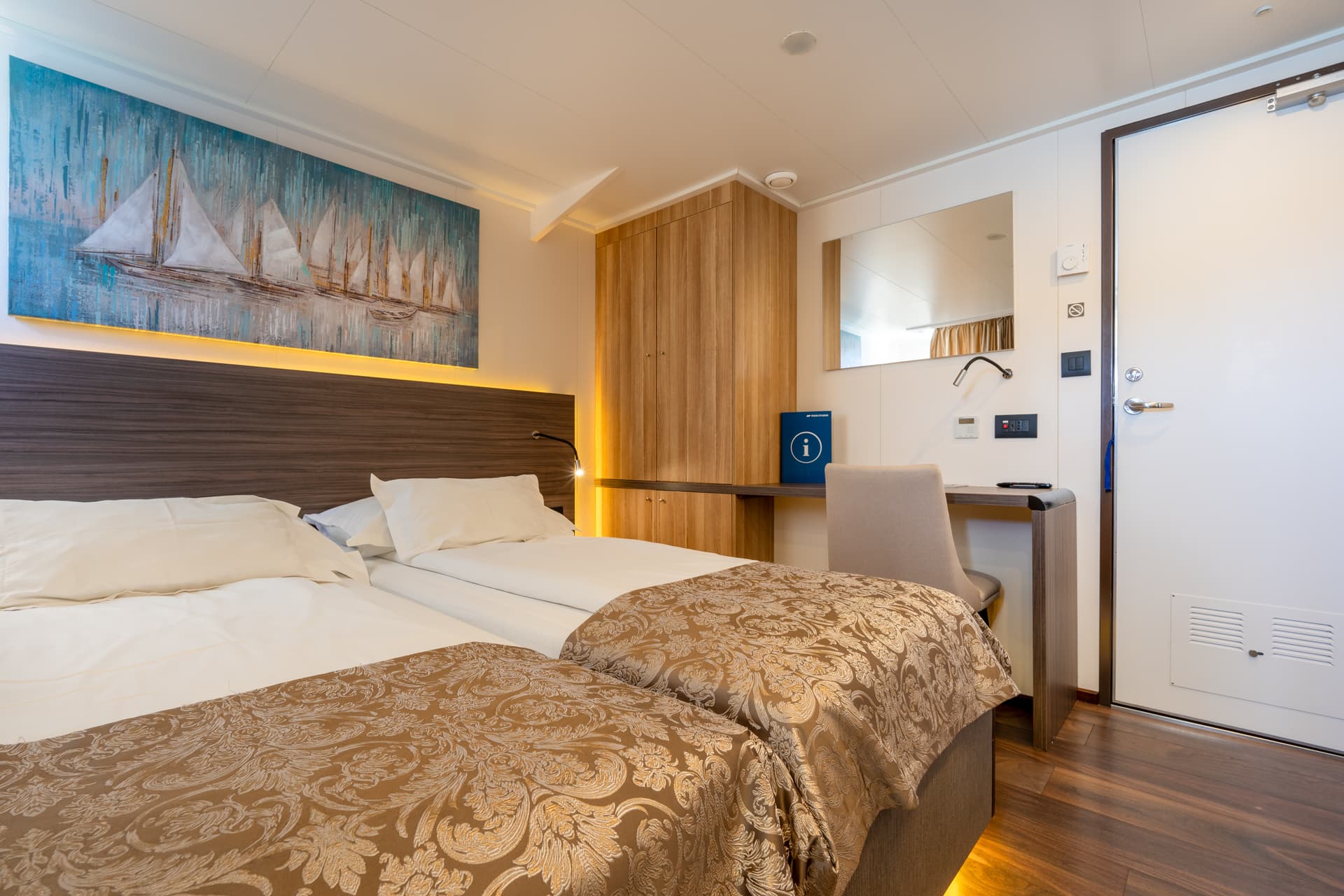 Main deck cabin with twin beds, wooden wardrobe, desk, and sailboat artwork on wall