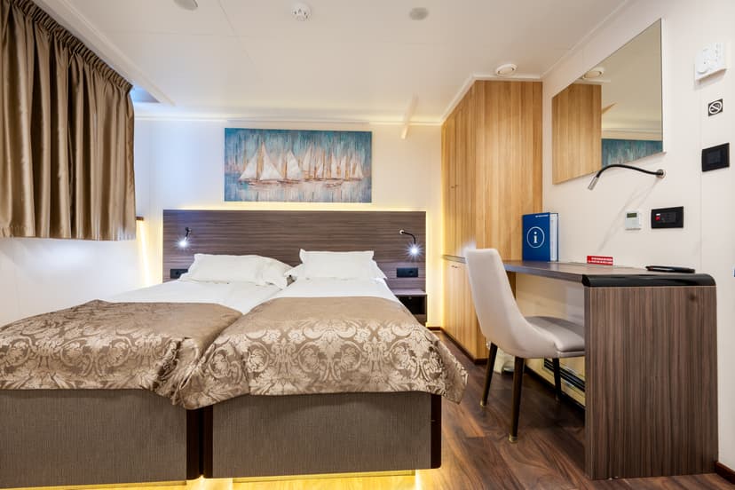 Ship cabin with twin beds, wooden desk, chair, and coastal wall art