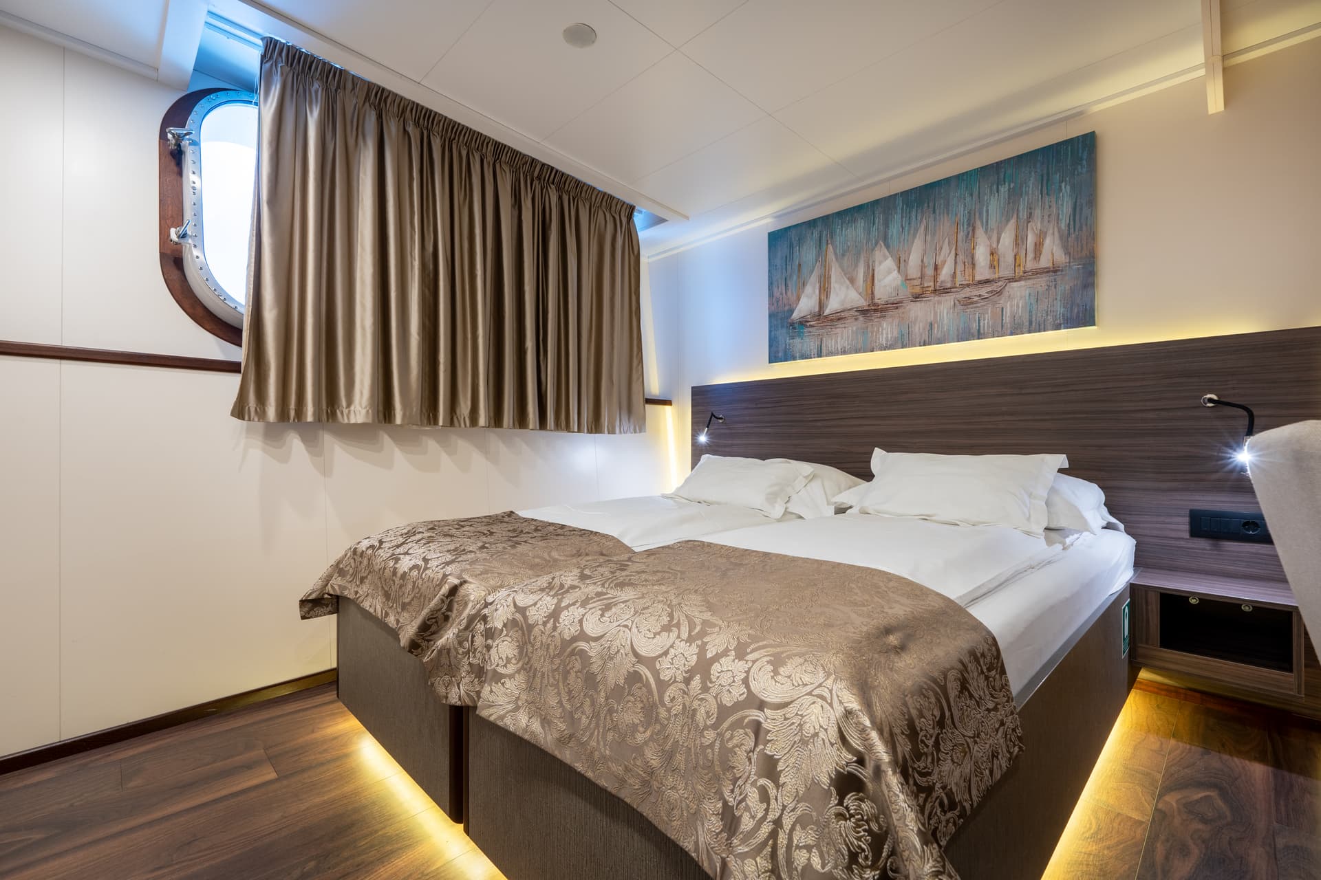 Main deck cabin bedroom with twin beds, porthole window, and sailboat artwork