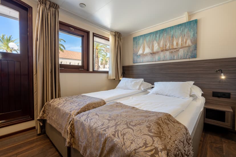 Main deck cabin with twin beds, wooden accents, and windows showing palm trees outside
