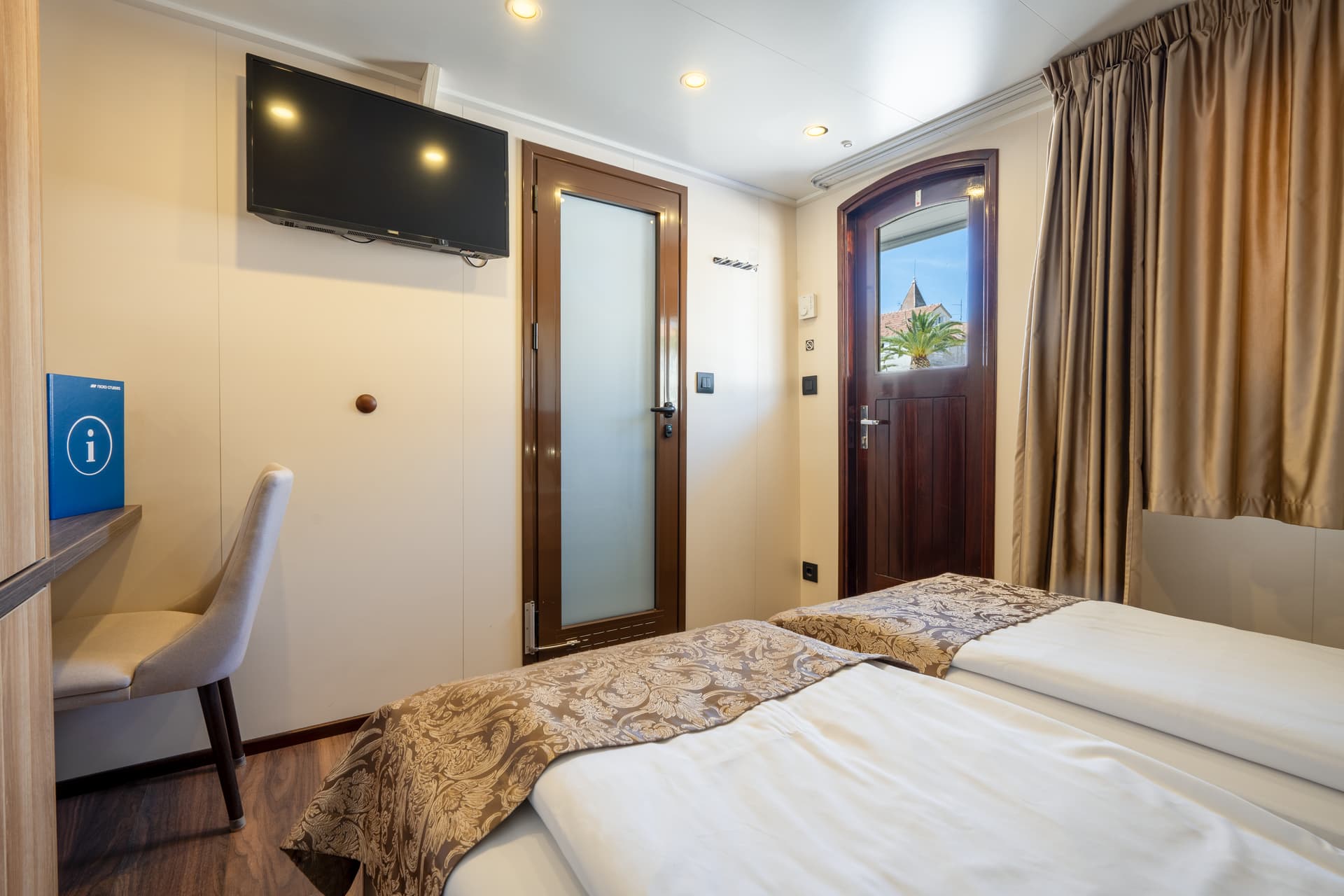 Main deck cabin interior with twin beds, desk, TV, and door to outside deck