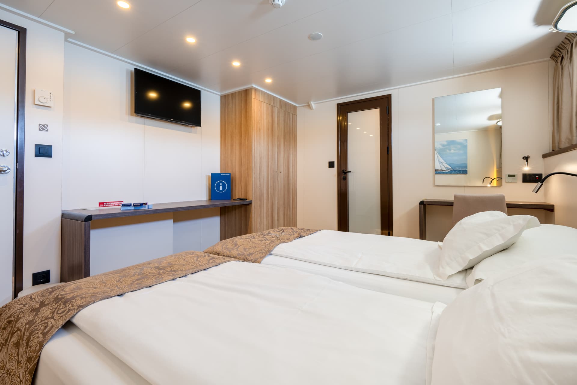 Standard cruise ship cabin with twin beds, desk, TV, and wardrobe