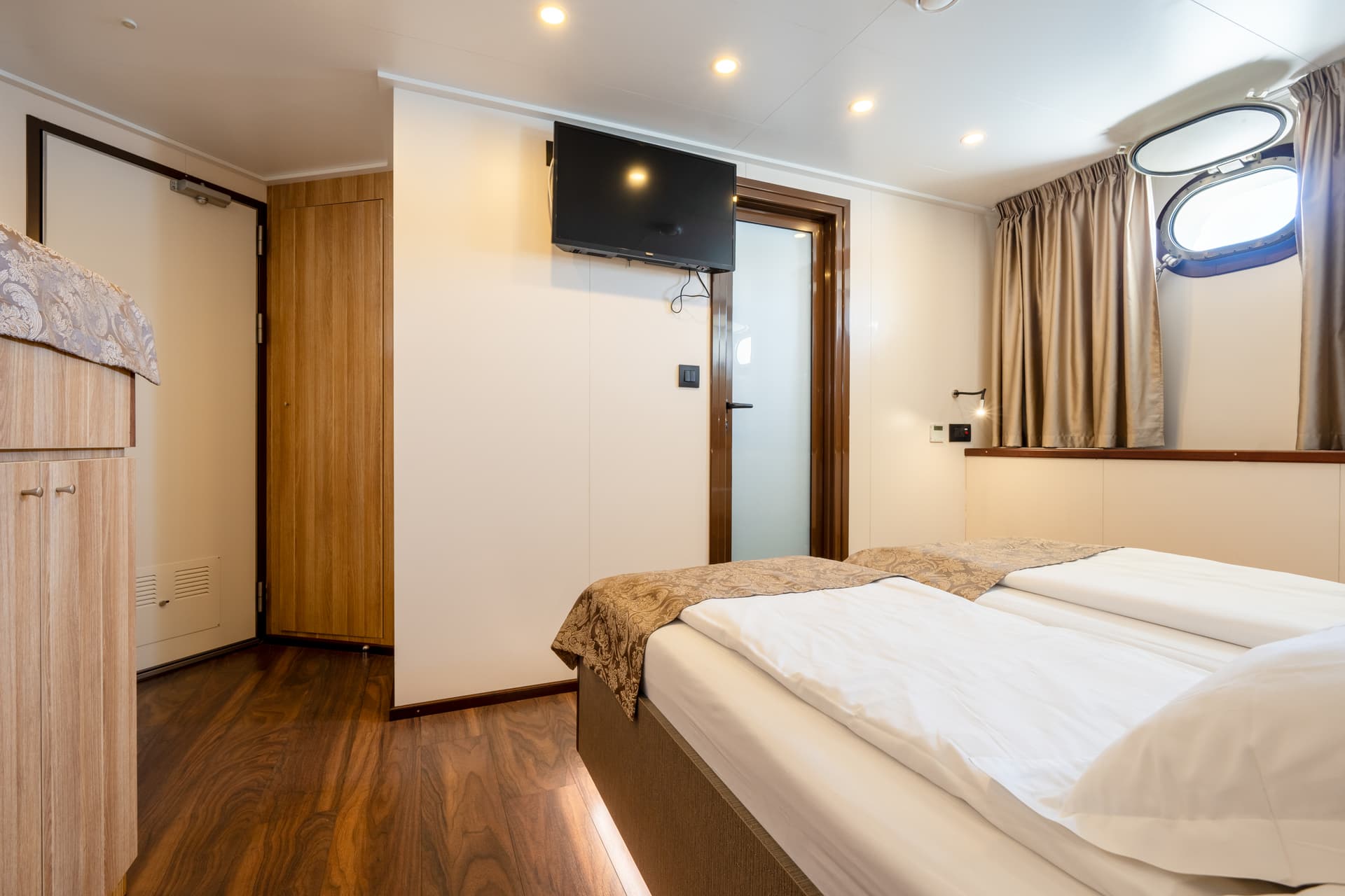 Standard cabin bedroom with twin beds and porthole window on a ship
