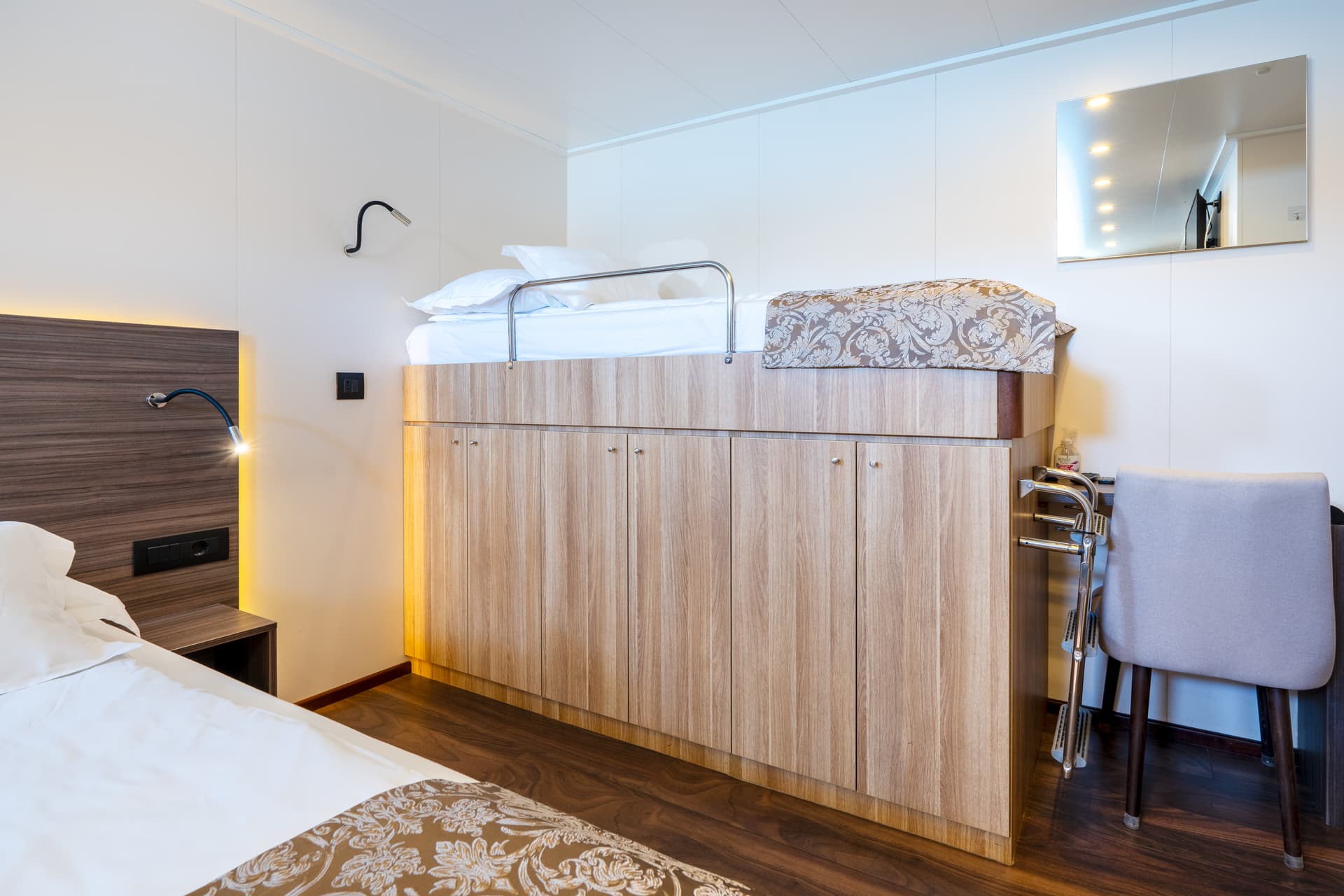 Ship cabin interior with bunk bed over wooden cabinets and desk chair